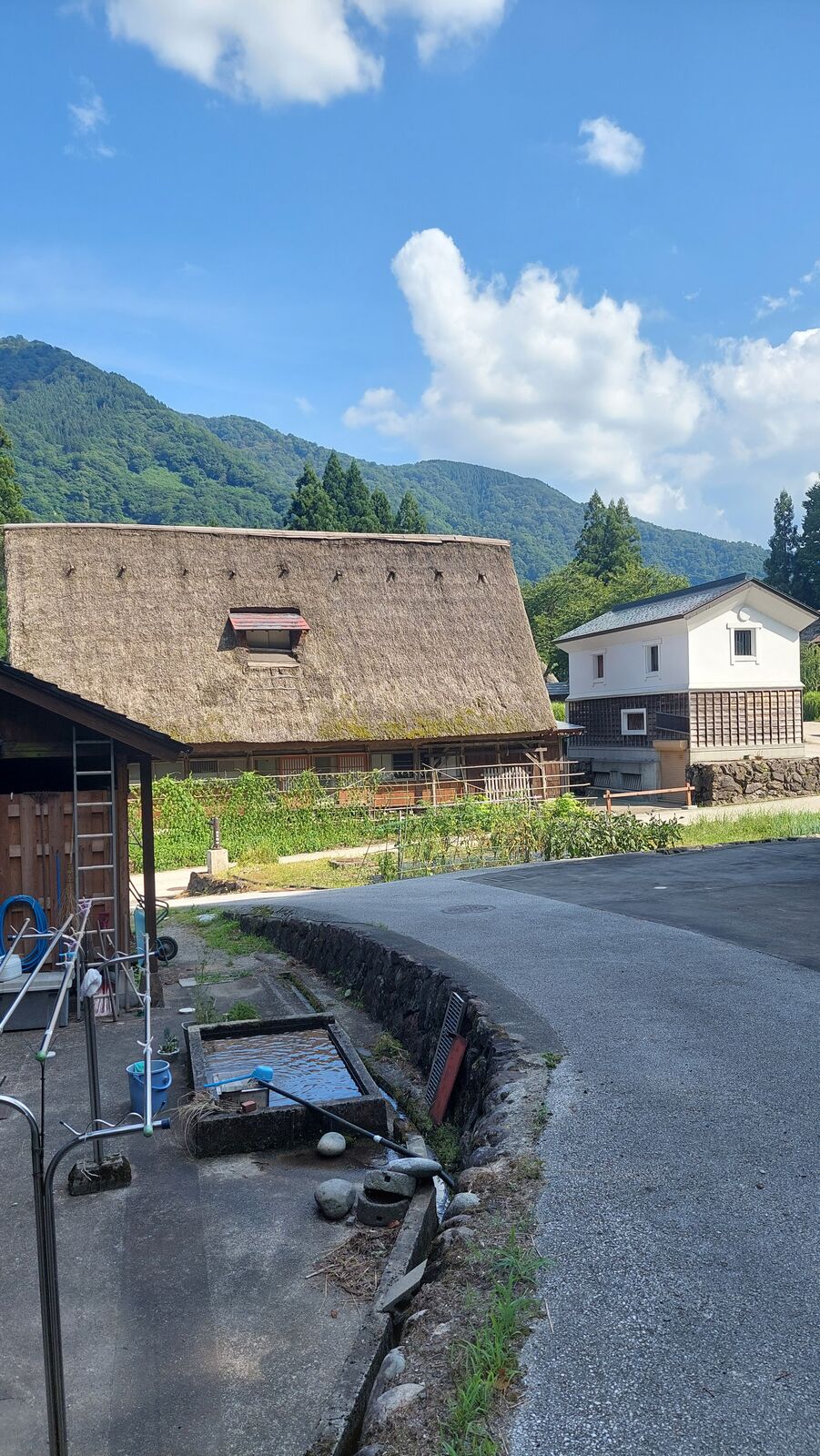 Village road with a gassho house, open water channel, and white kura storehouse