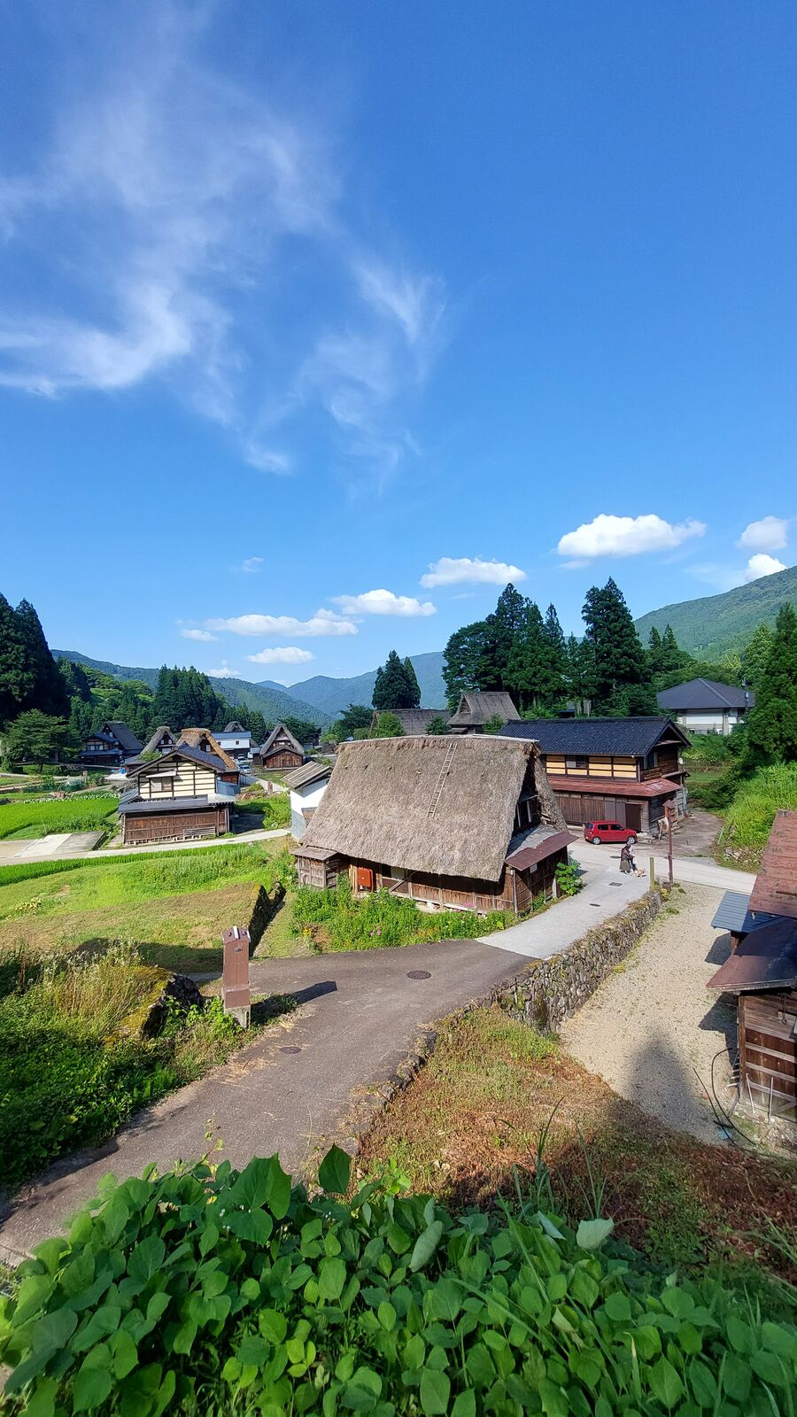 Village road with houses on both sides, a red car parked among the gassho-zukuri buildings