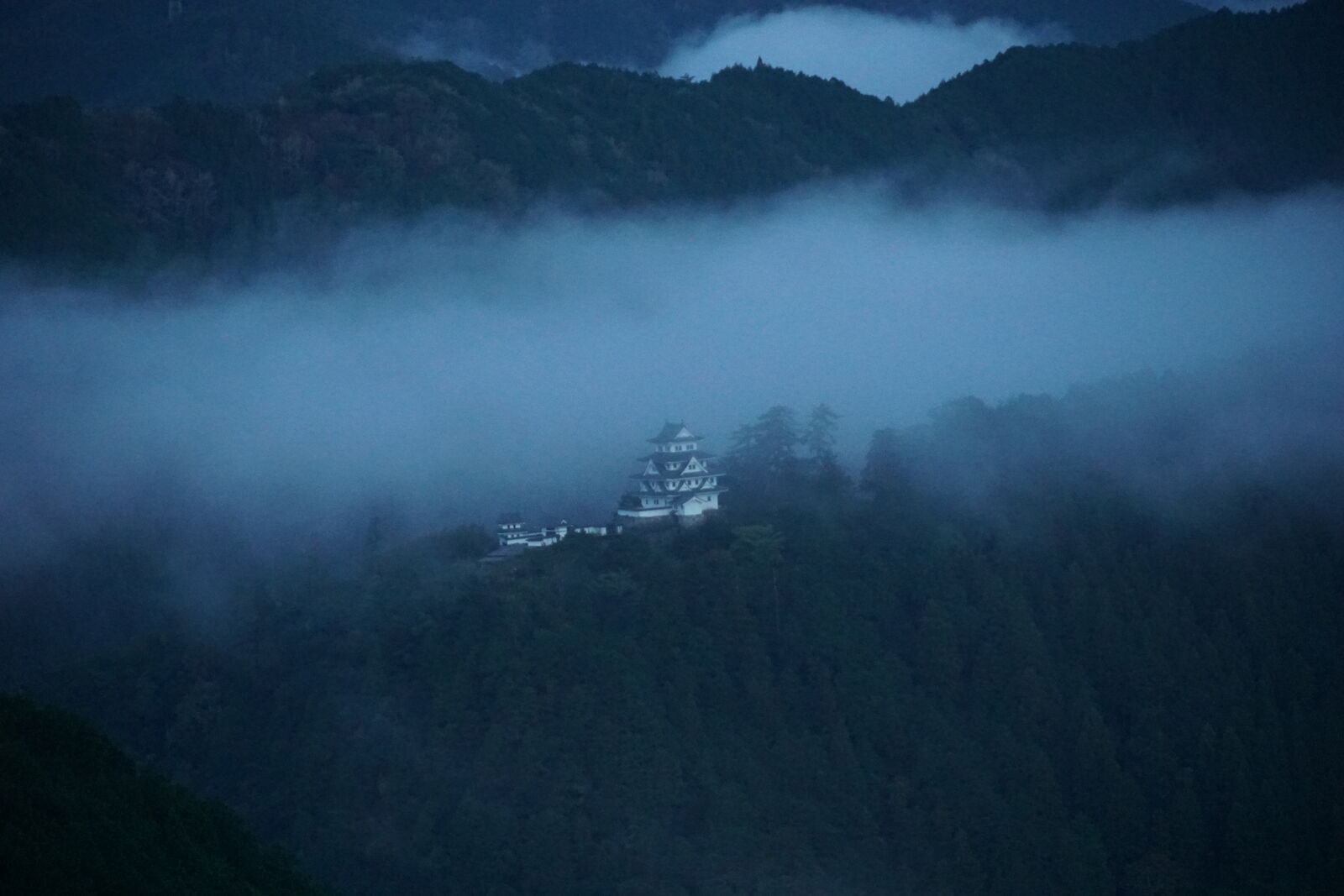 Gujo Hachiman Castle in blue pre-dawn light, emerging from thick fog that fills the valley