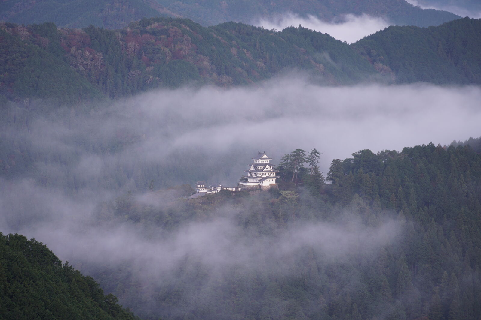 Castle with cloud swirls clearing around it, revealing the valley below