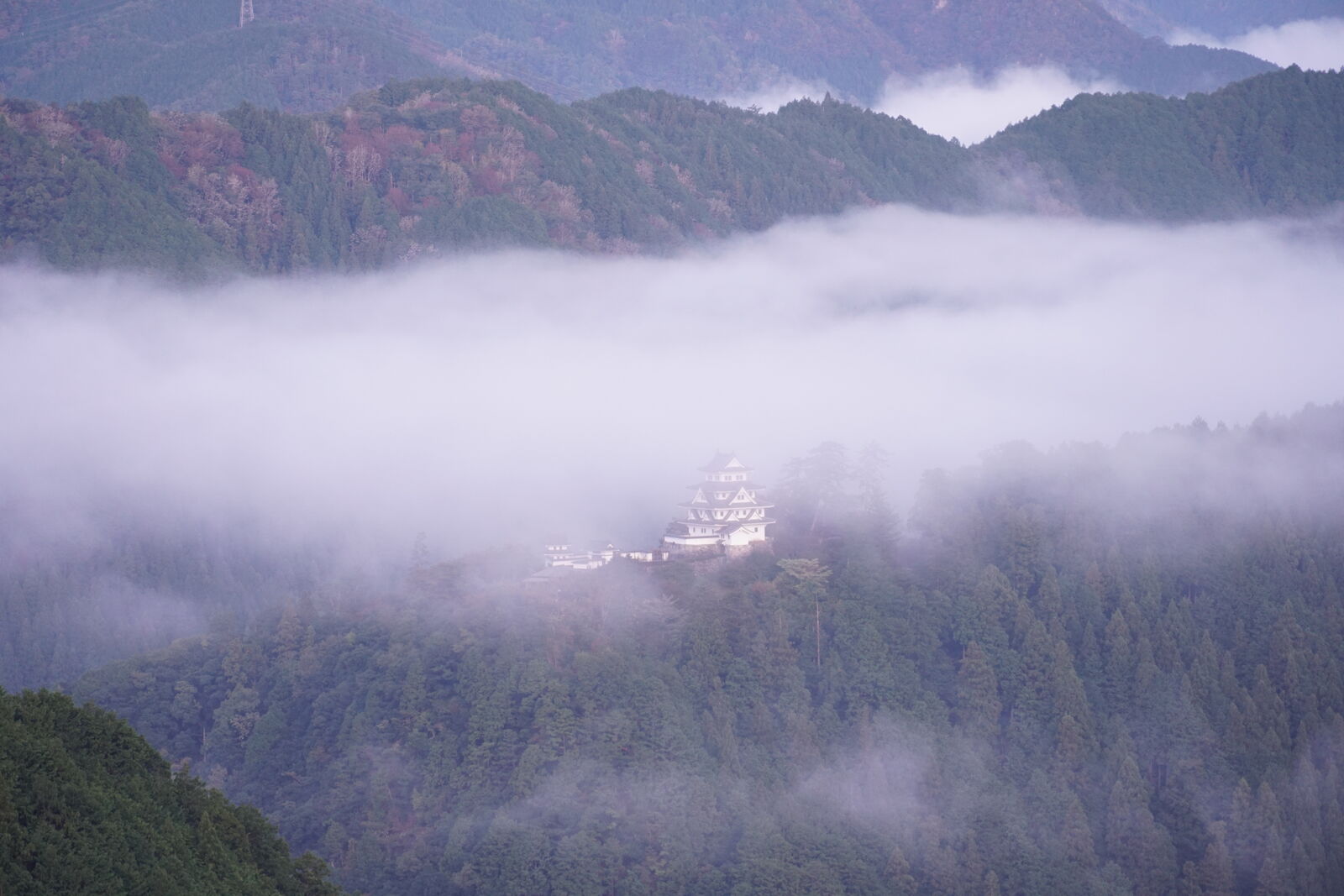 Castle standing in sharp contrast above the dense white cloud sea filling the valley