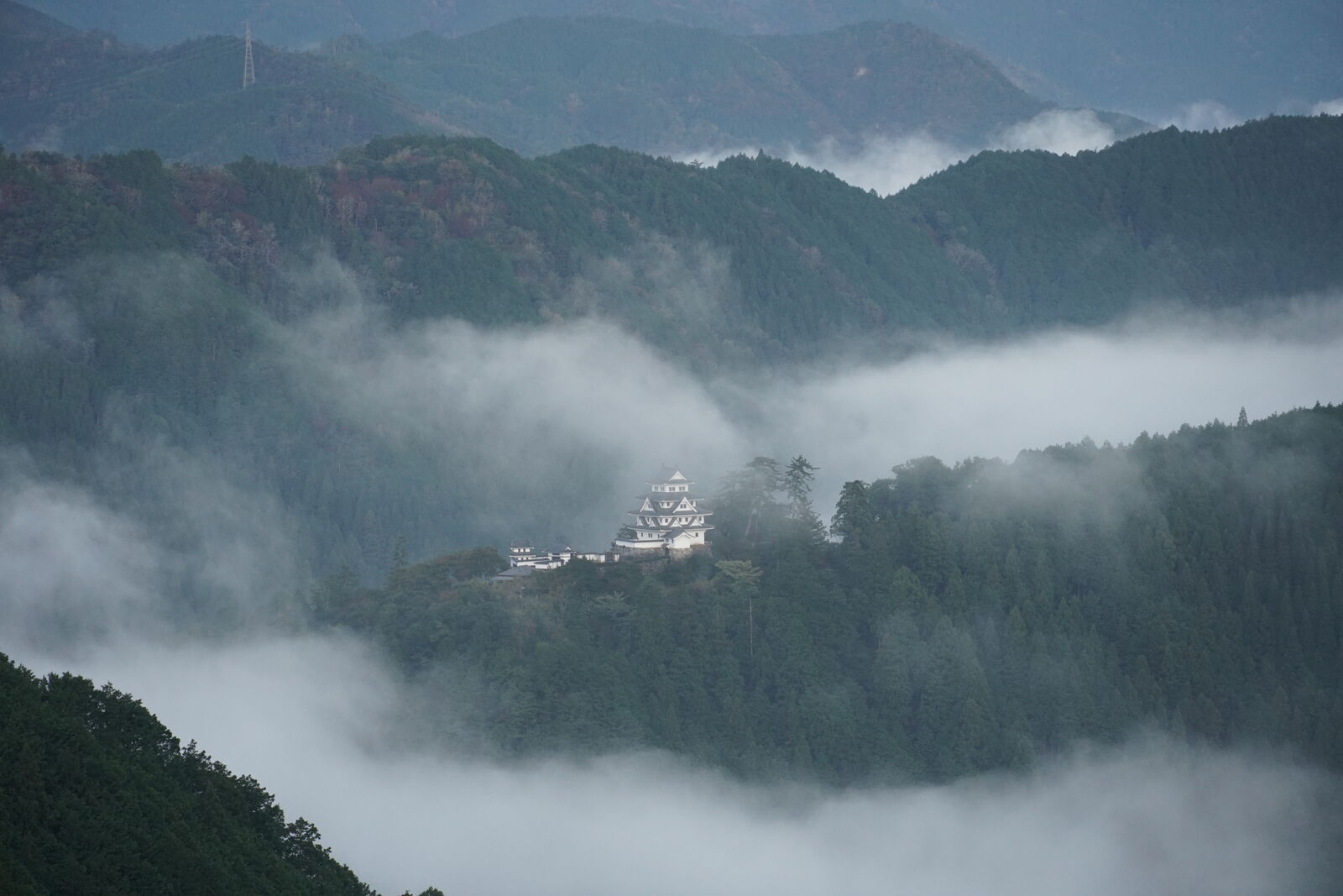 Gujo Hachiman Castle with morning clouds beginning to thin, revealing forested slopes below
