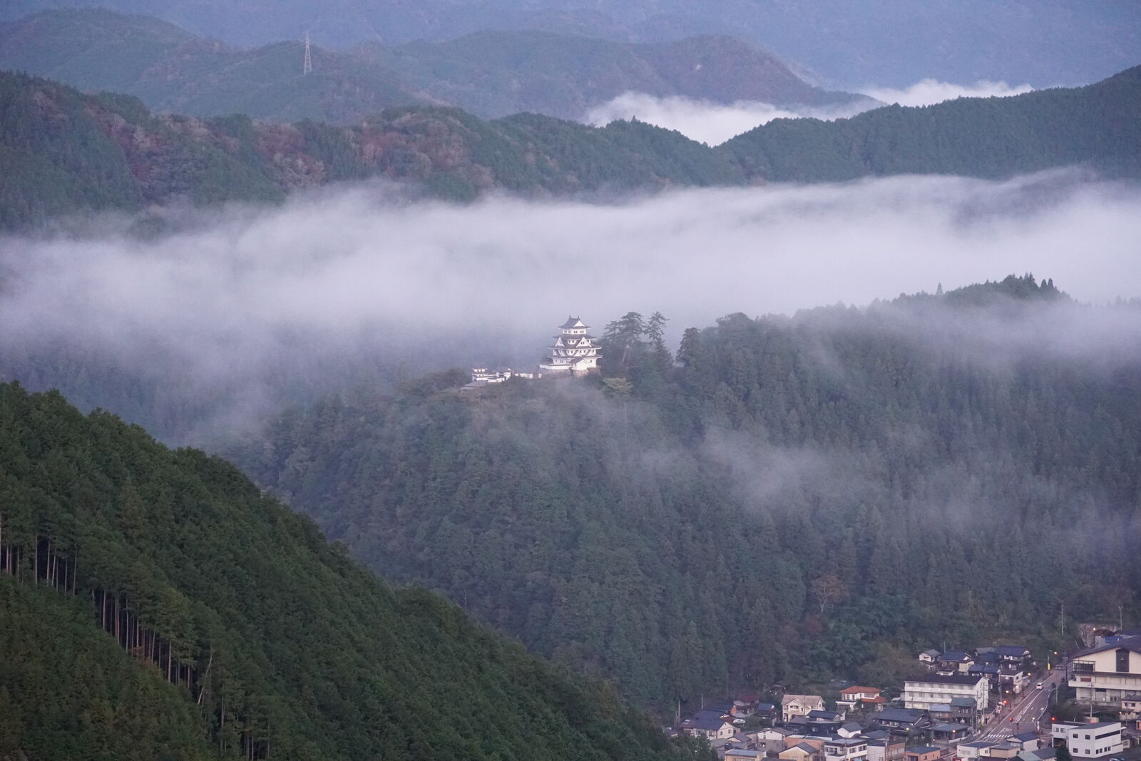 Layered cloud formations around the castle with mountains receding into the distance