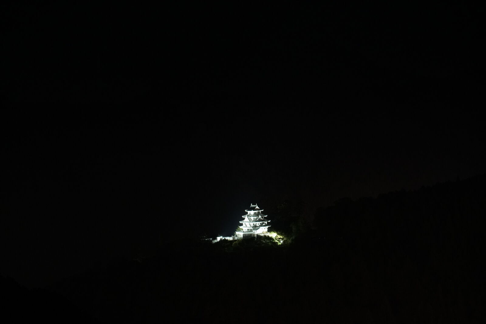 Gujo Hachiman Castle illuminated white against the dark mountain at night