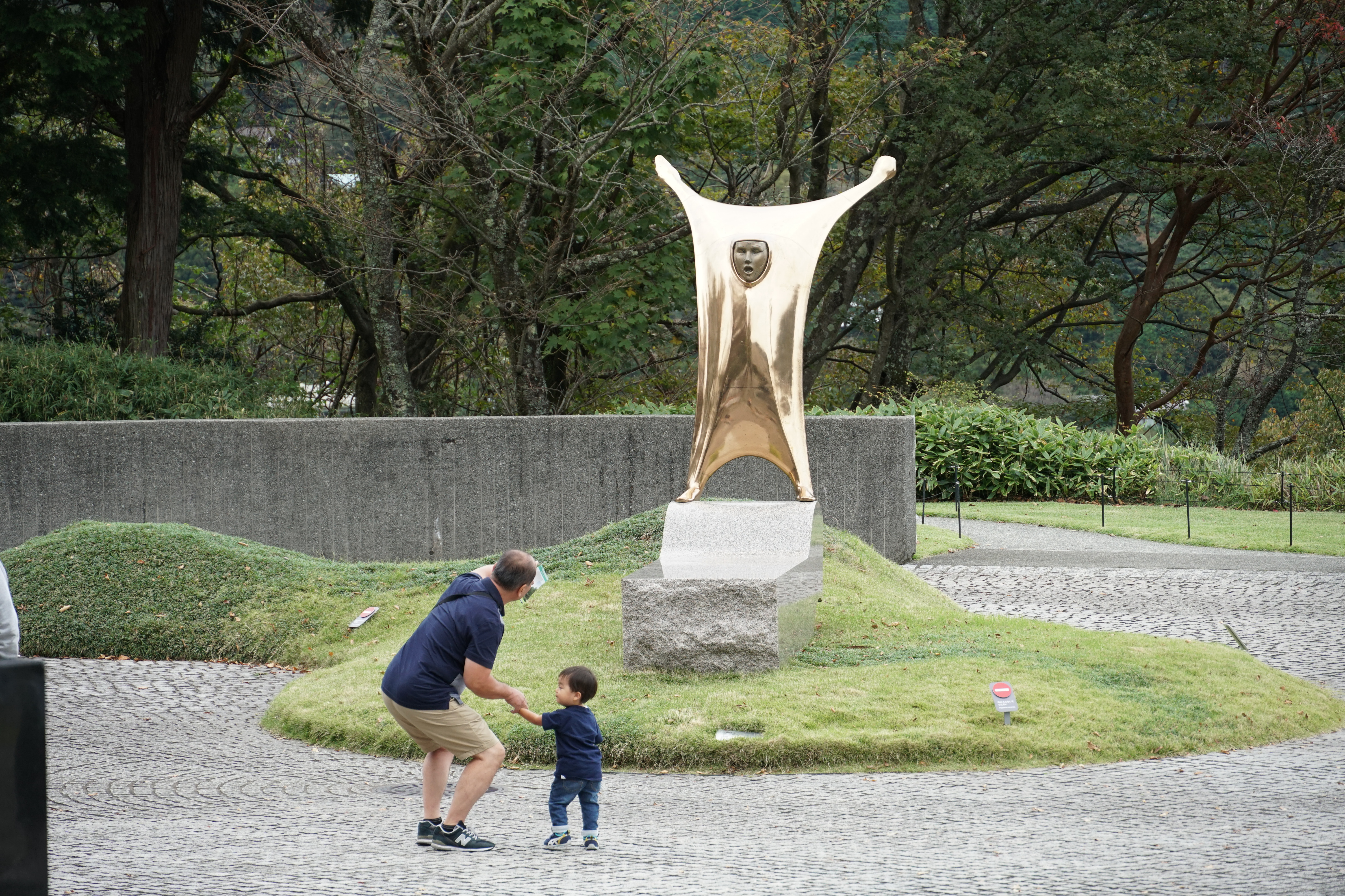 Father and toddler in front of a golden figure sculpture