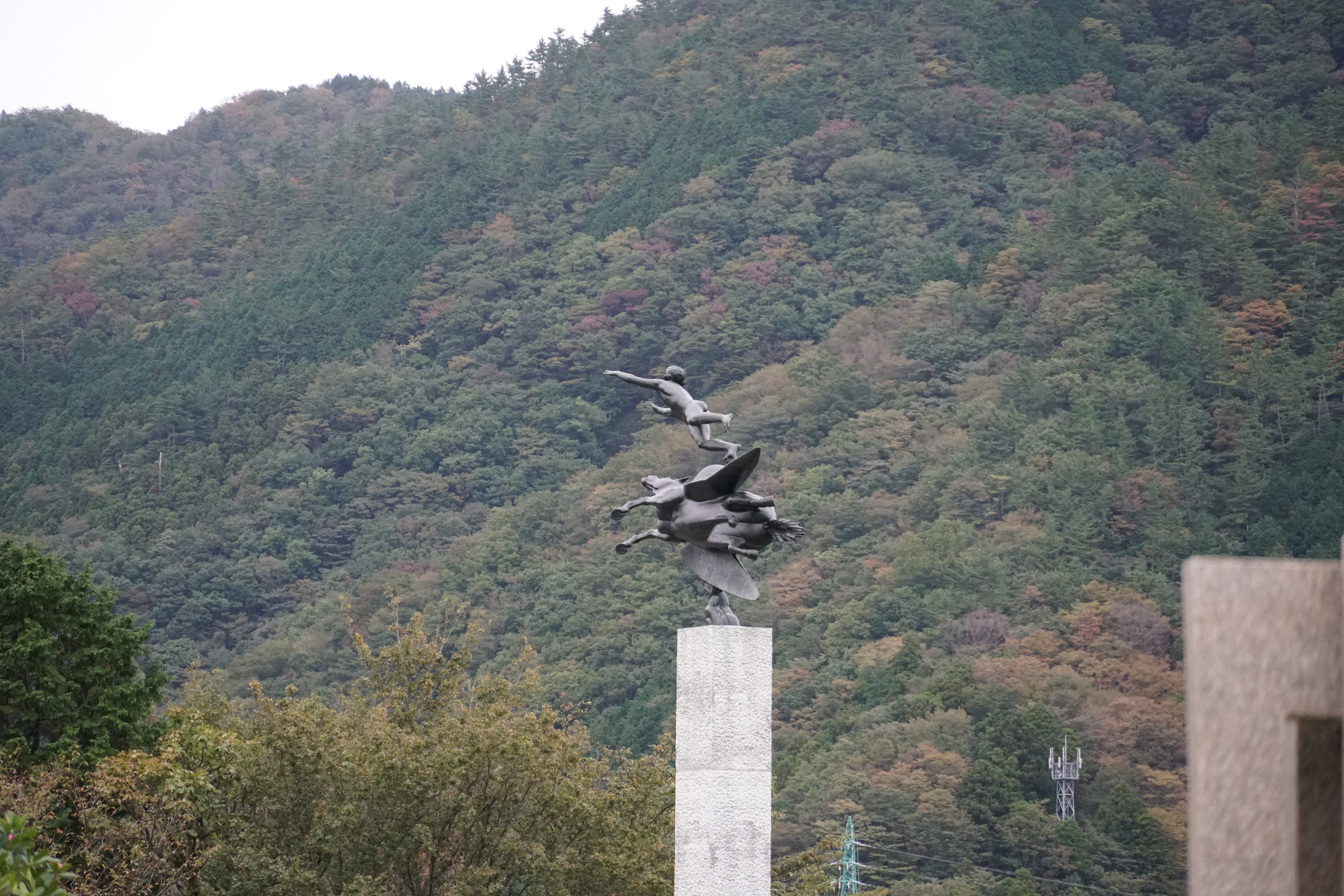 Bronze figure on a tall pedestal silhouetted against the mountain backdrop