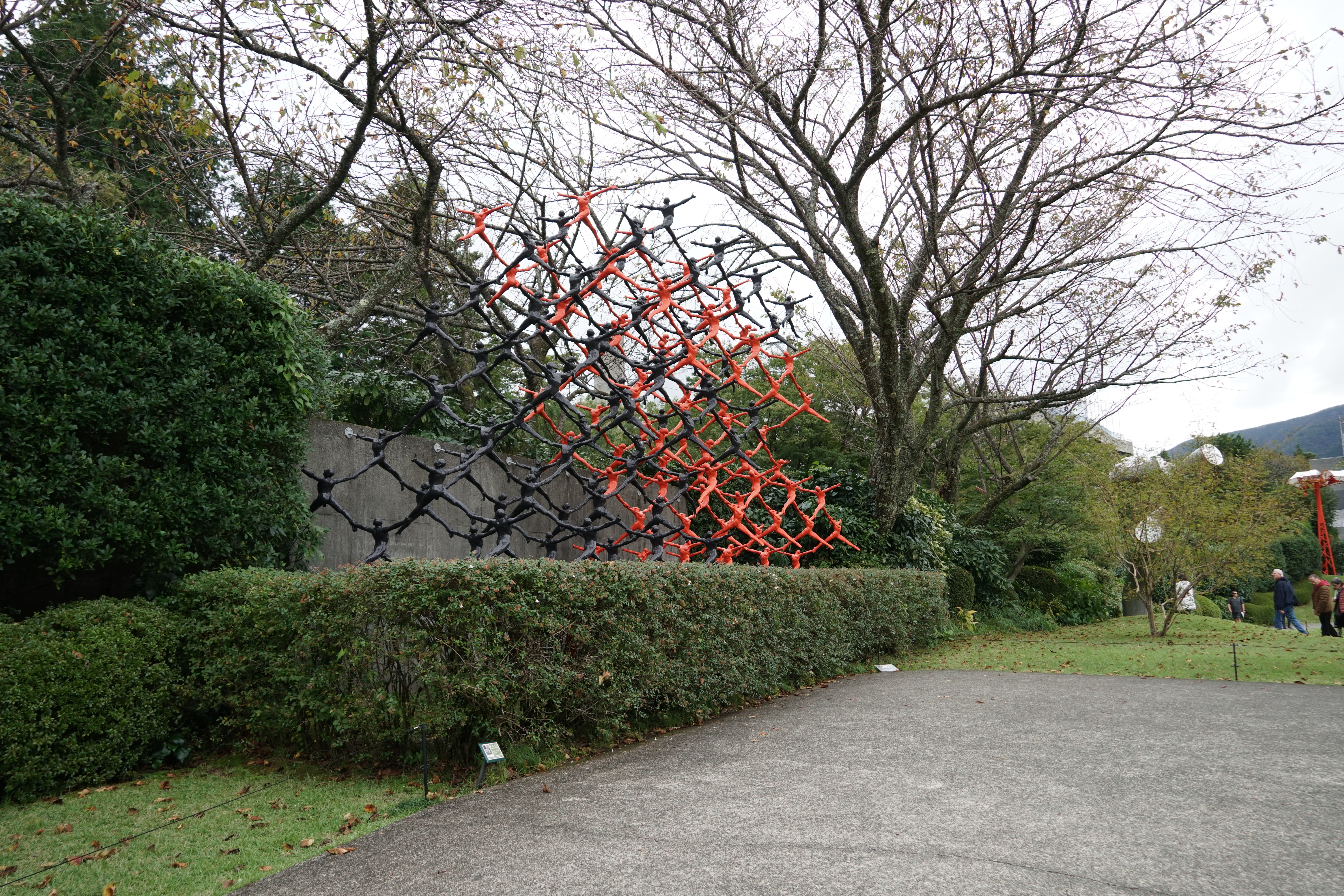 Red and black geometric mesh lattice sculpture rising against autumn trees