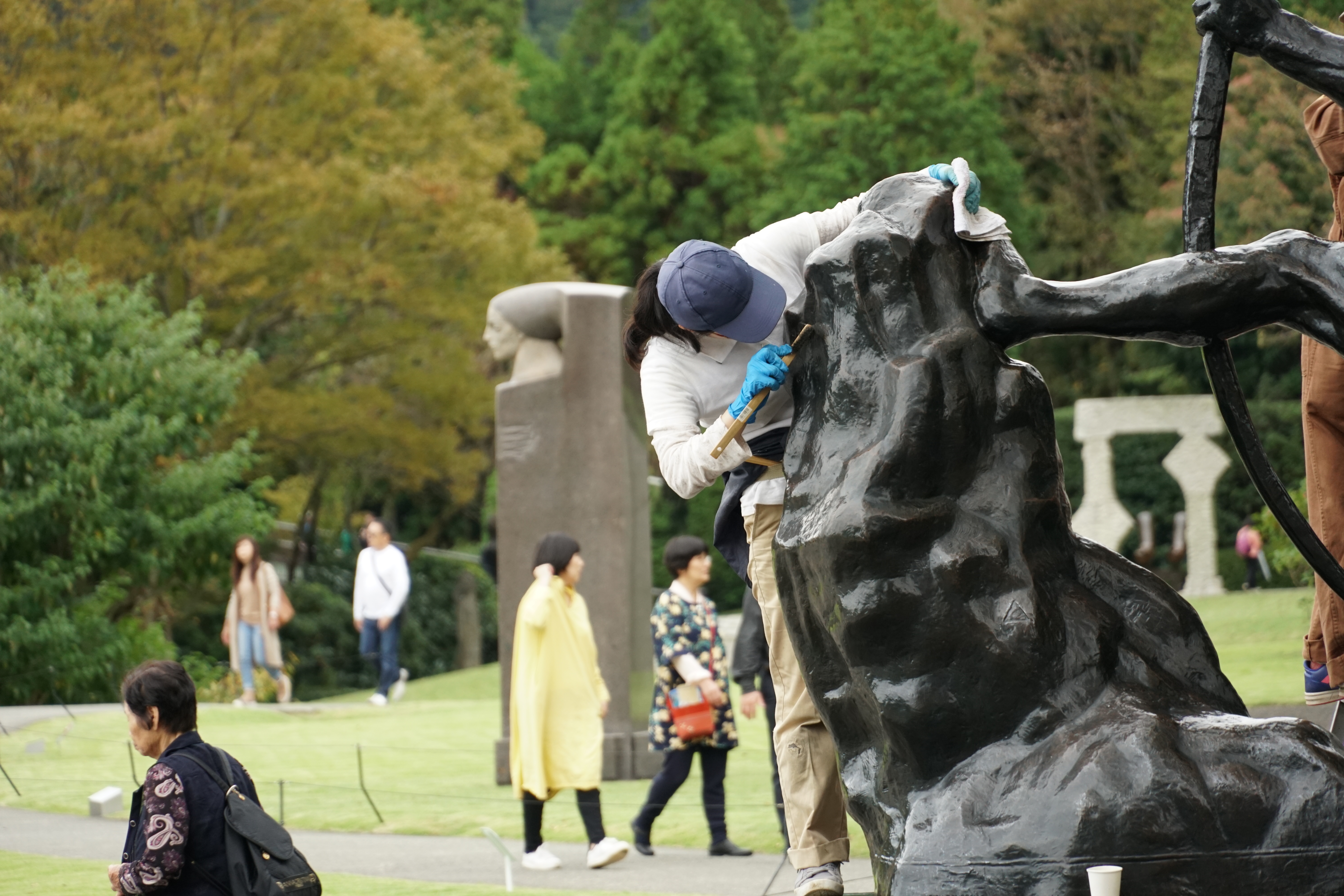 Staff maintaining sculpture with visitors and autumn trees