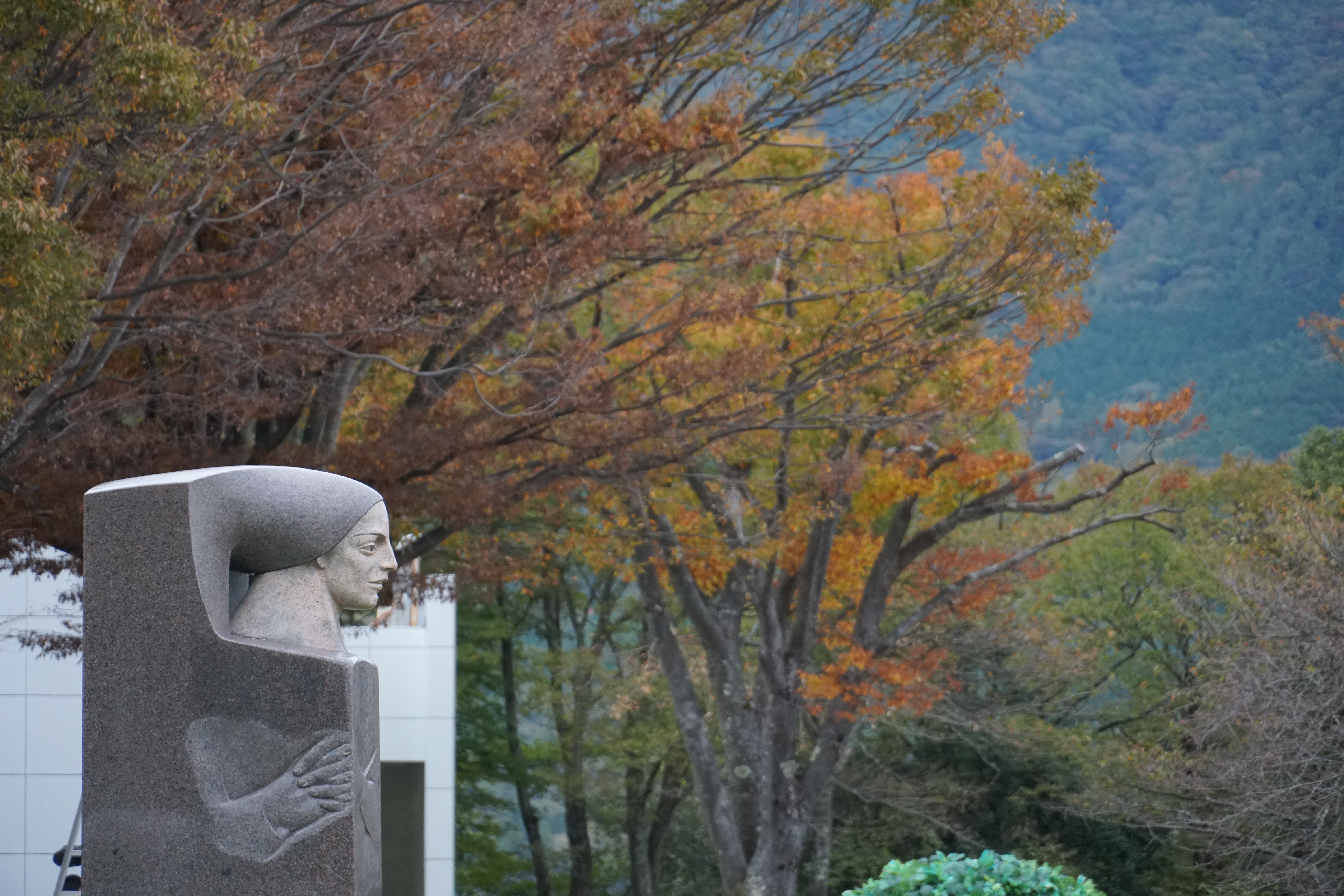 Carved stone head sculpture framed by golden and orange autumn foliage with mountains behind