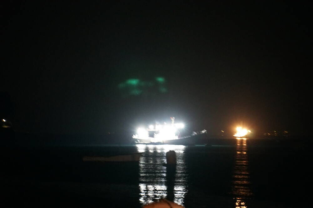 A fishing boat lit up at night in Heda harbour, its lights and green glow reflecting on the dark water