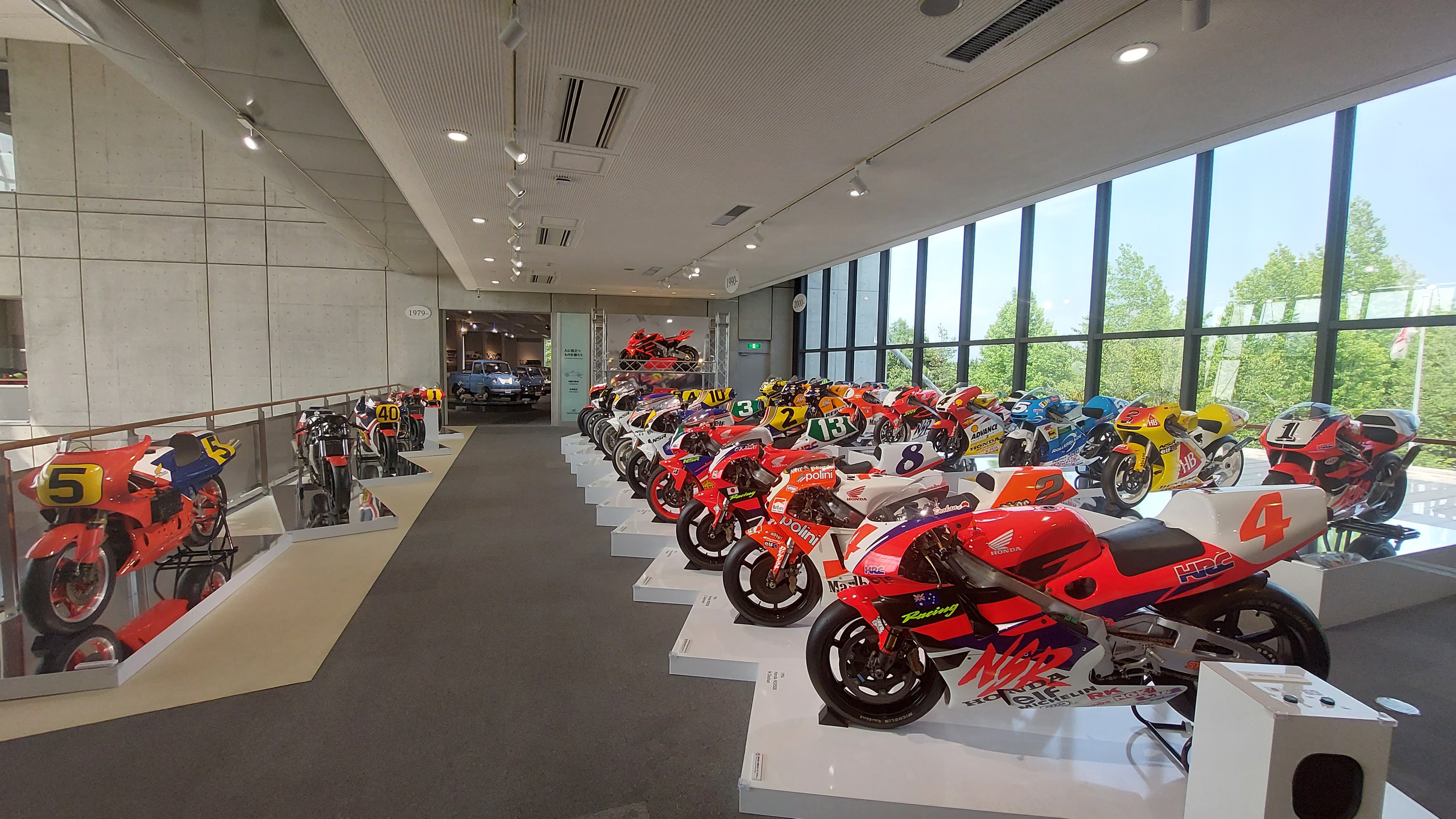 Panoramic view of the entire MotoGP motorcycle collection, dozens of bikes from every era lined up along the window wall