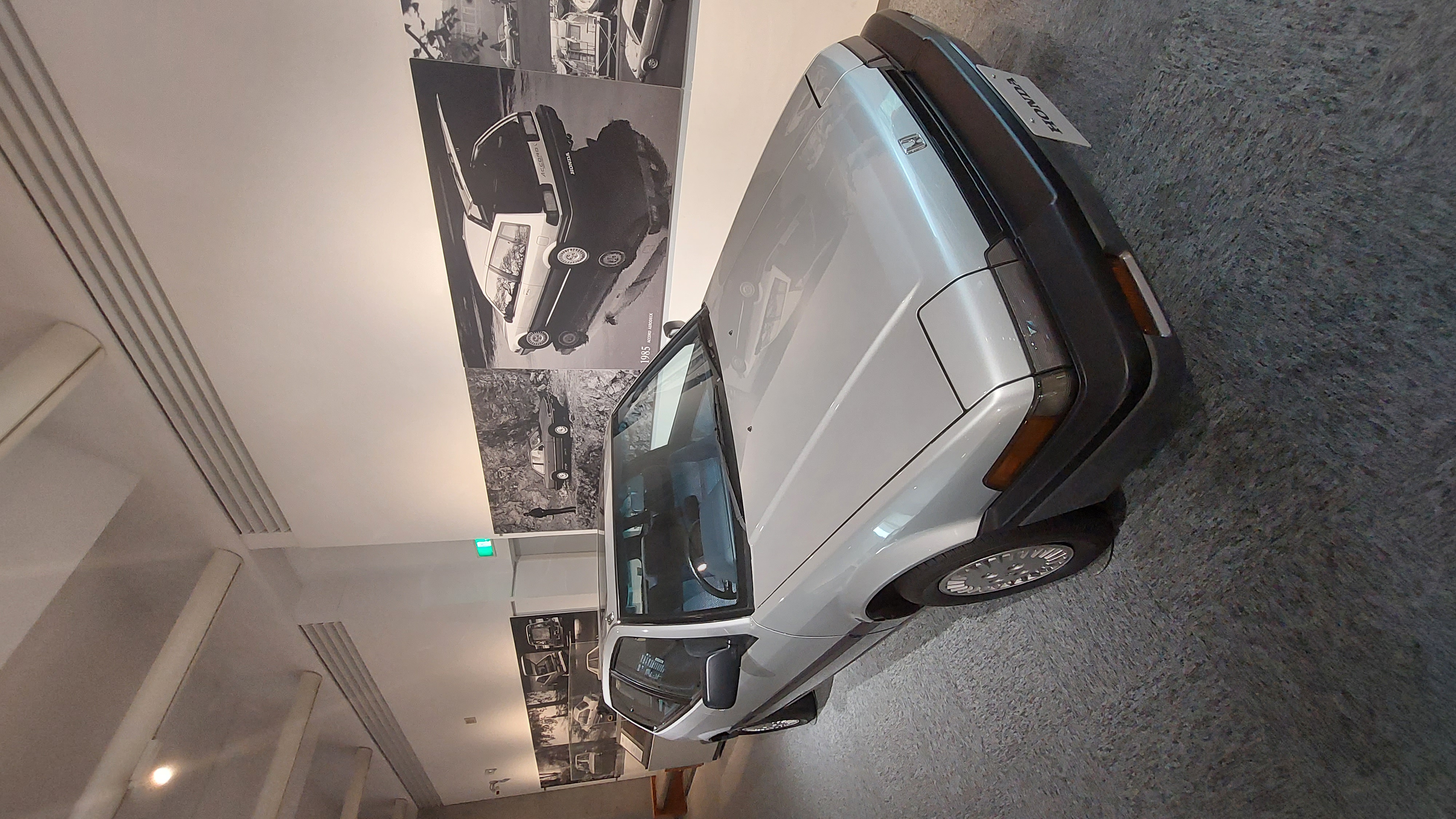 Silver Honda Accord with period photographs on the wall behind it, the car that proved Honda could build a proper sedan