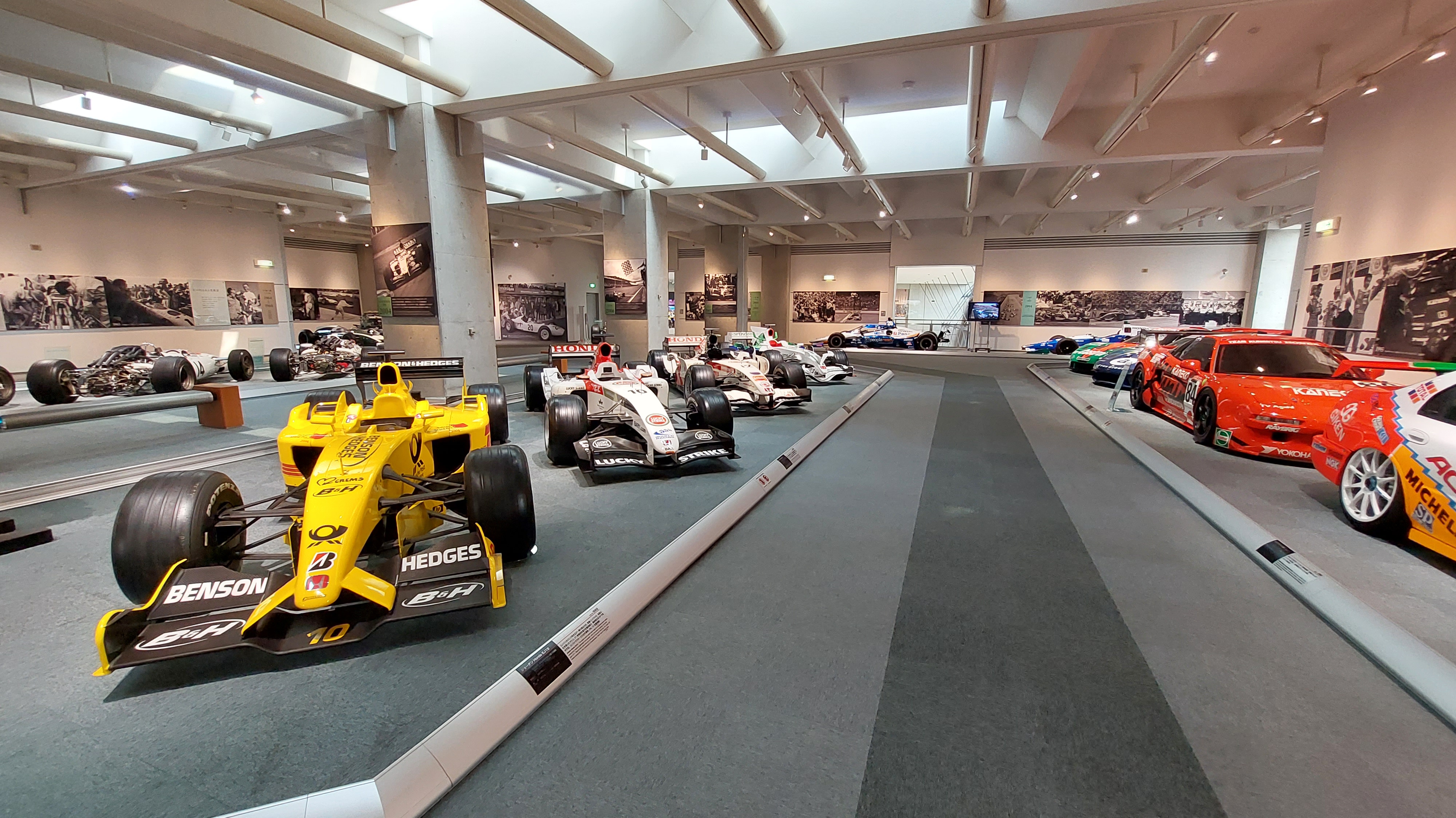 The racing hall in full panorama: F1 cars, Super GT machines, IndyCars, all in one massive space with historic photos on the walls