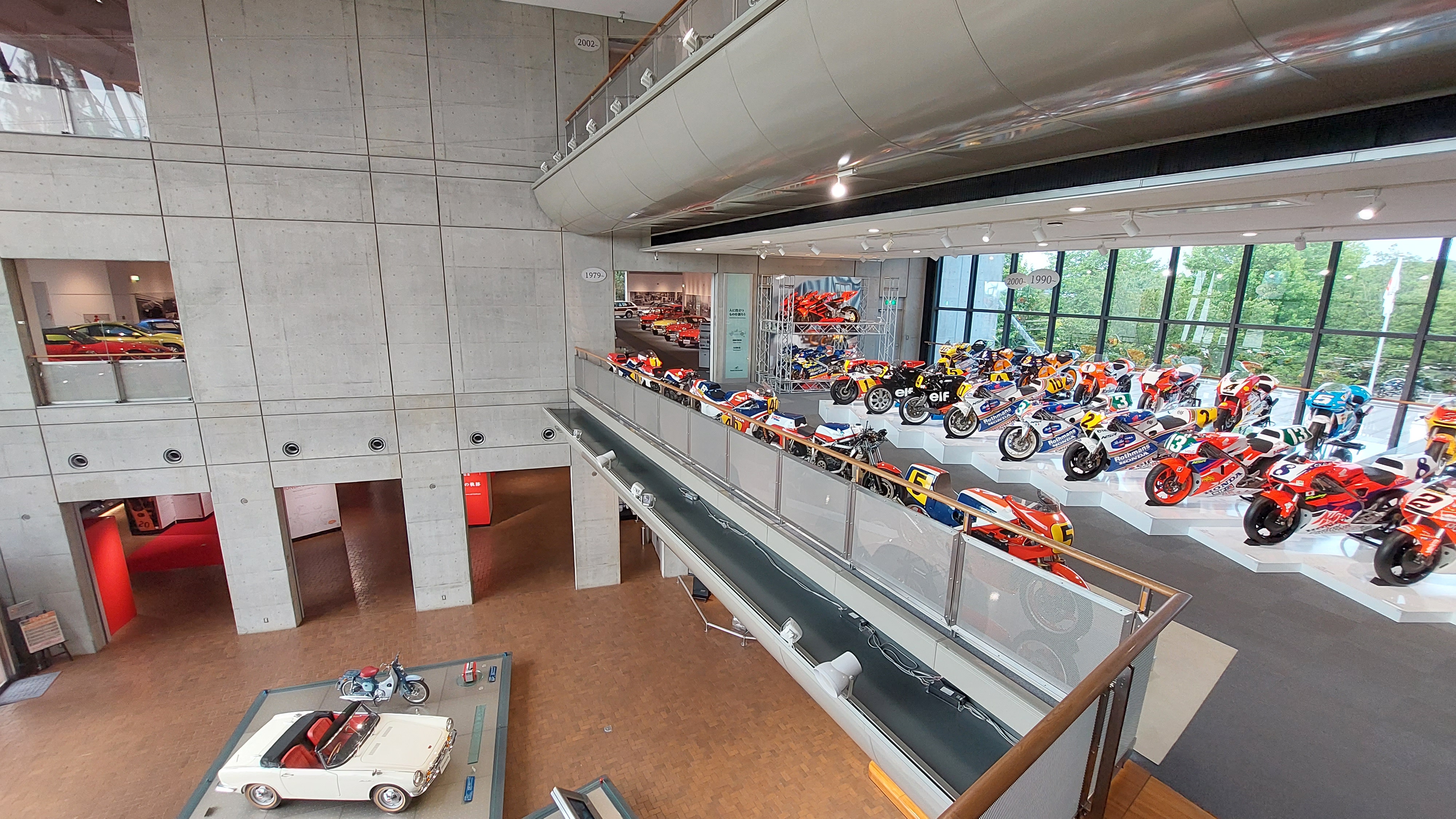 Full multi-story overview of the Honda Collection Hall, concrete and glass architecture with bikes on the mezzanine and cars below