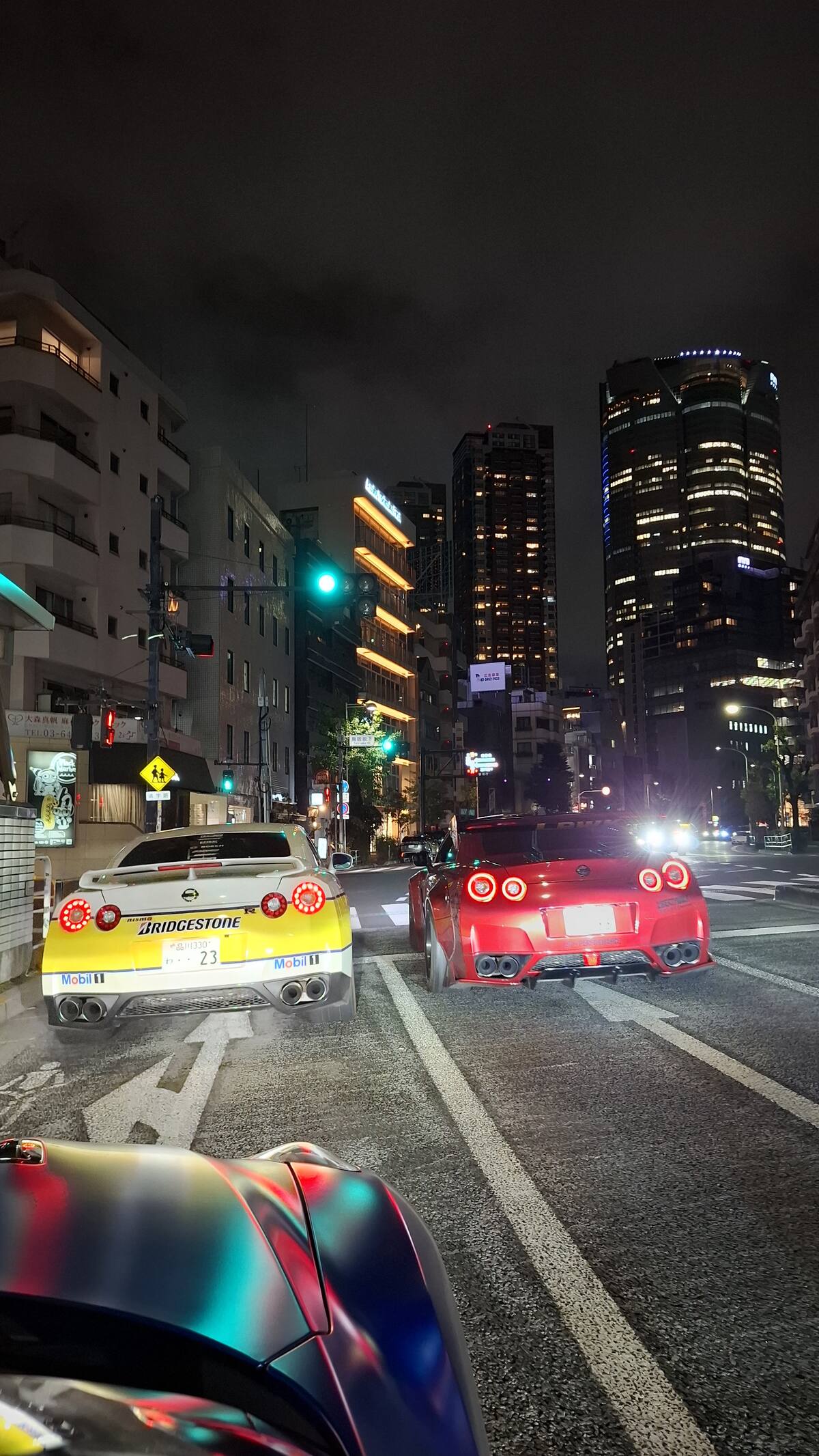 Red GT-R and Bridgestone #23 at a Tokyo intersection with skyscrapers
