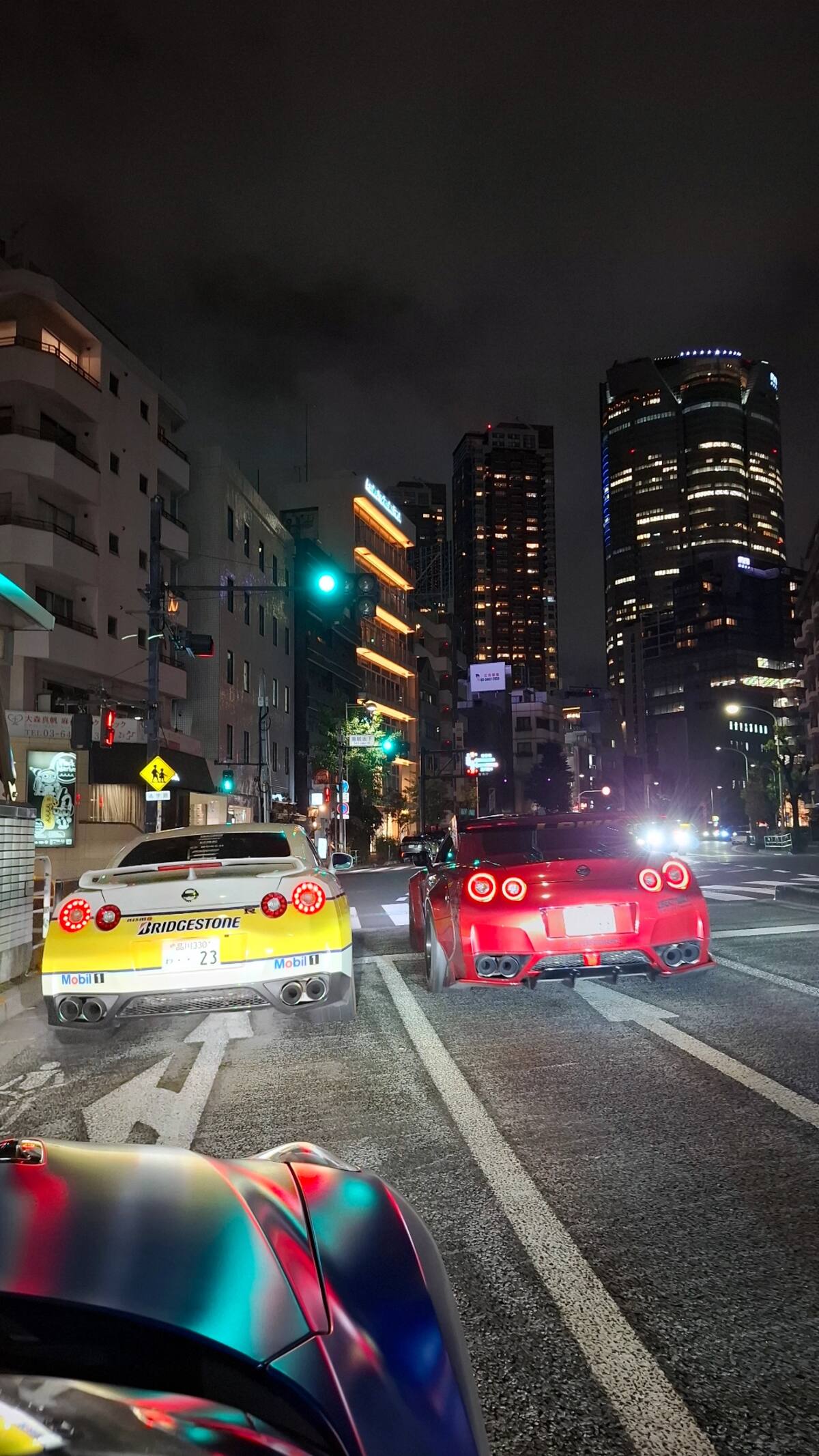 Both GT-Rs from behind driving through Tokyo with illuminated skyscrapers
