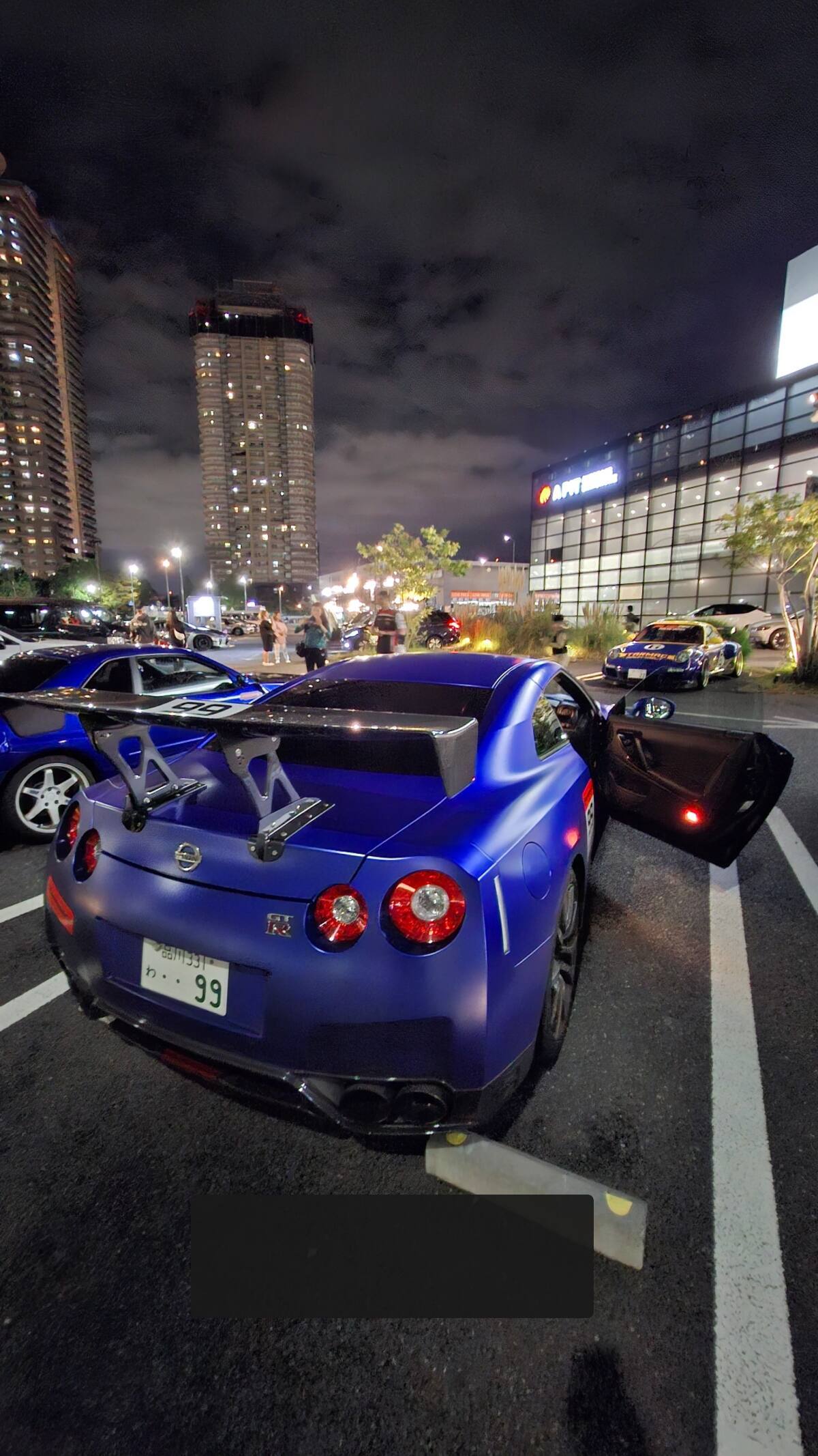 Blue GT-R #99 rear view at Daikoku PA with dramatic night sky and tower