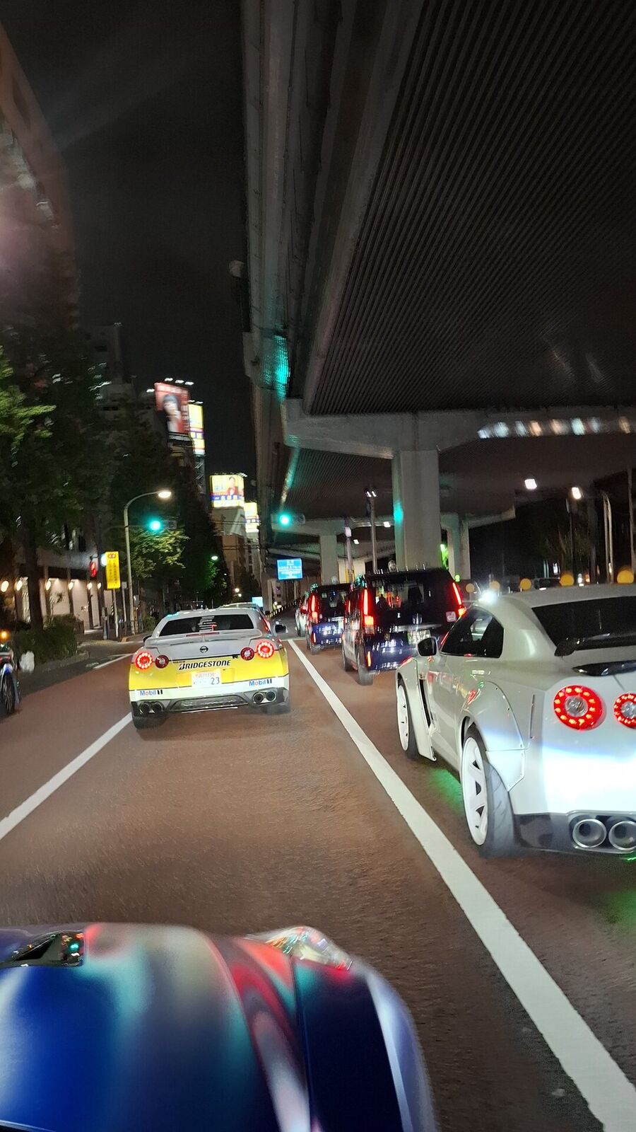 Multiple GT-Rs and the Bridgestone car lined up at a Tokyo intersection, showing the scale of the convoy
