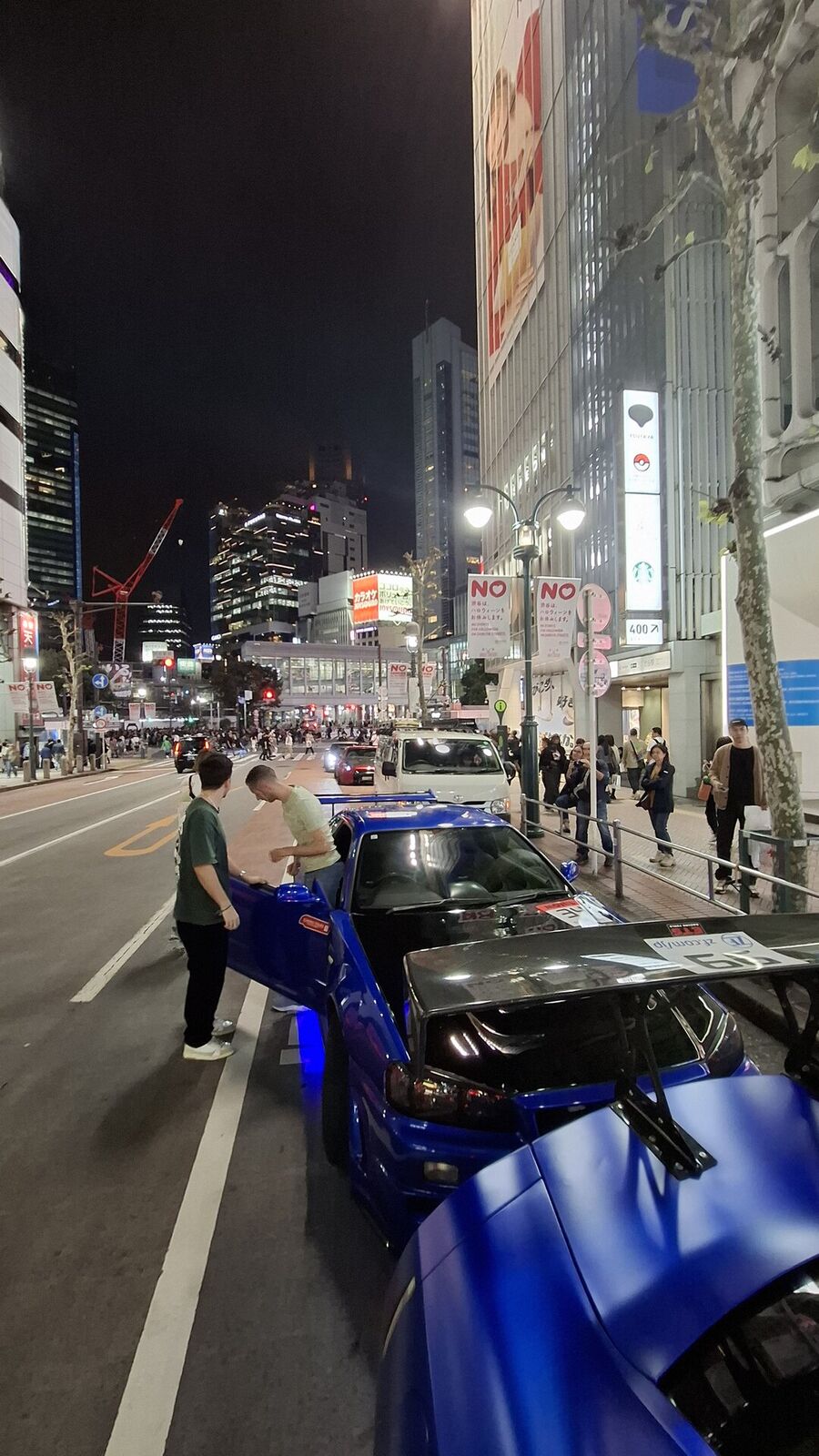 The Daikoku PA atmosphere: people photographing the blue GT-R, cars lined up under the PA lighting, the energy of Japan's most famous car meet spot