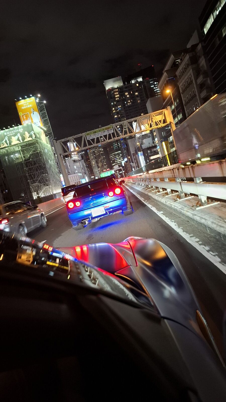 GT-R rear view on a Tokyo elevated road at night, city lights and construction crane creating an urban backdrop