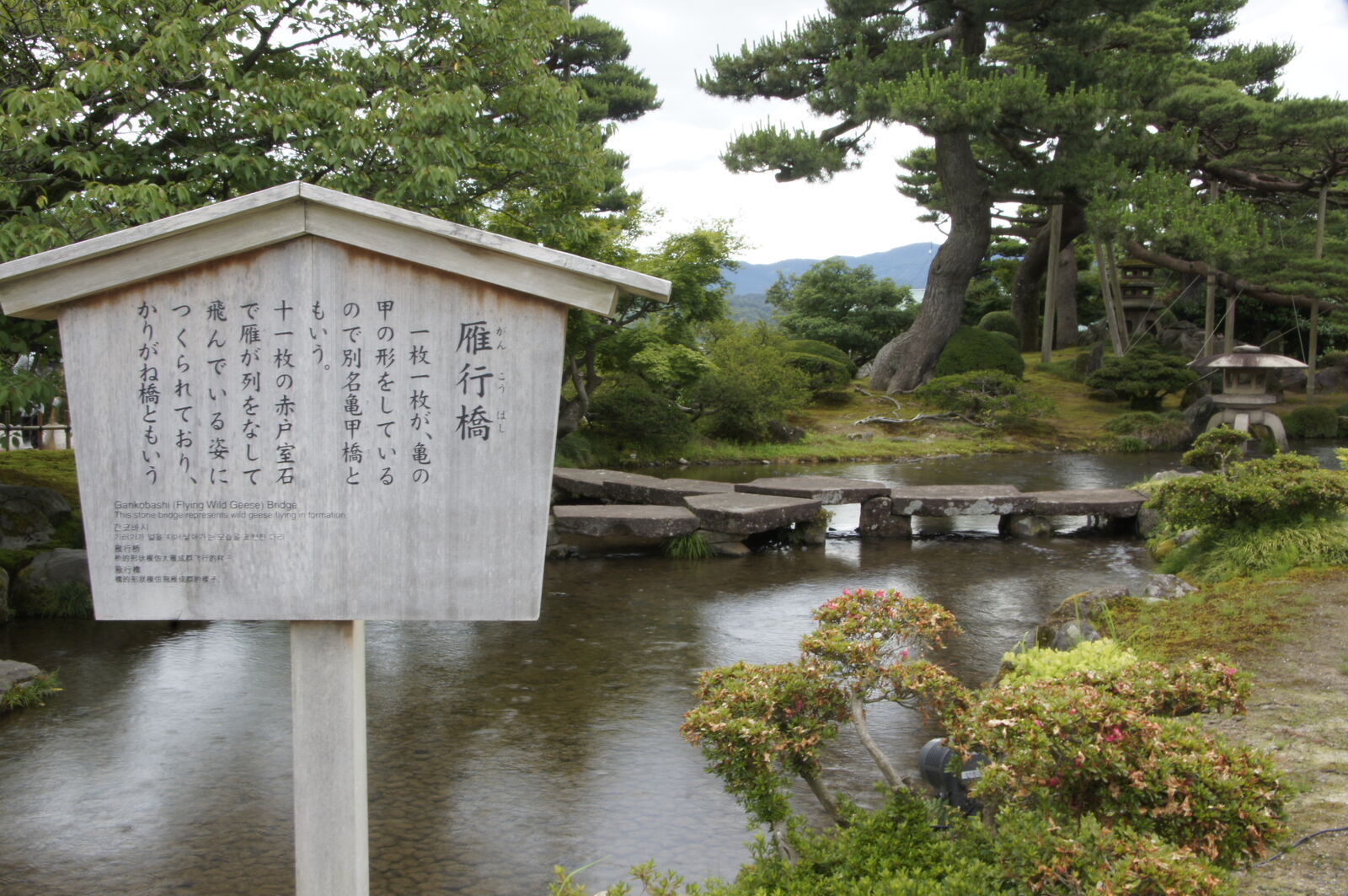 Ganko-bashi Flying Geese Bridge info sign with stone bridge and pines behind