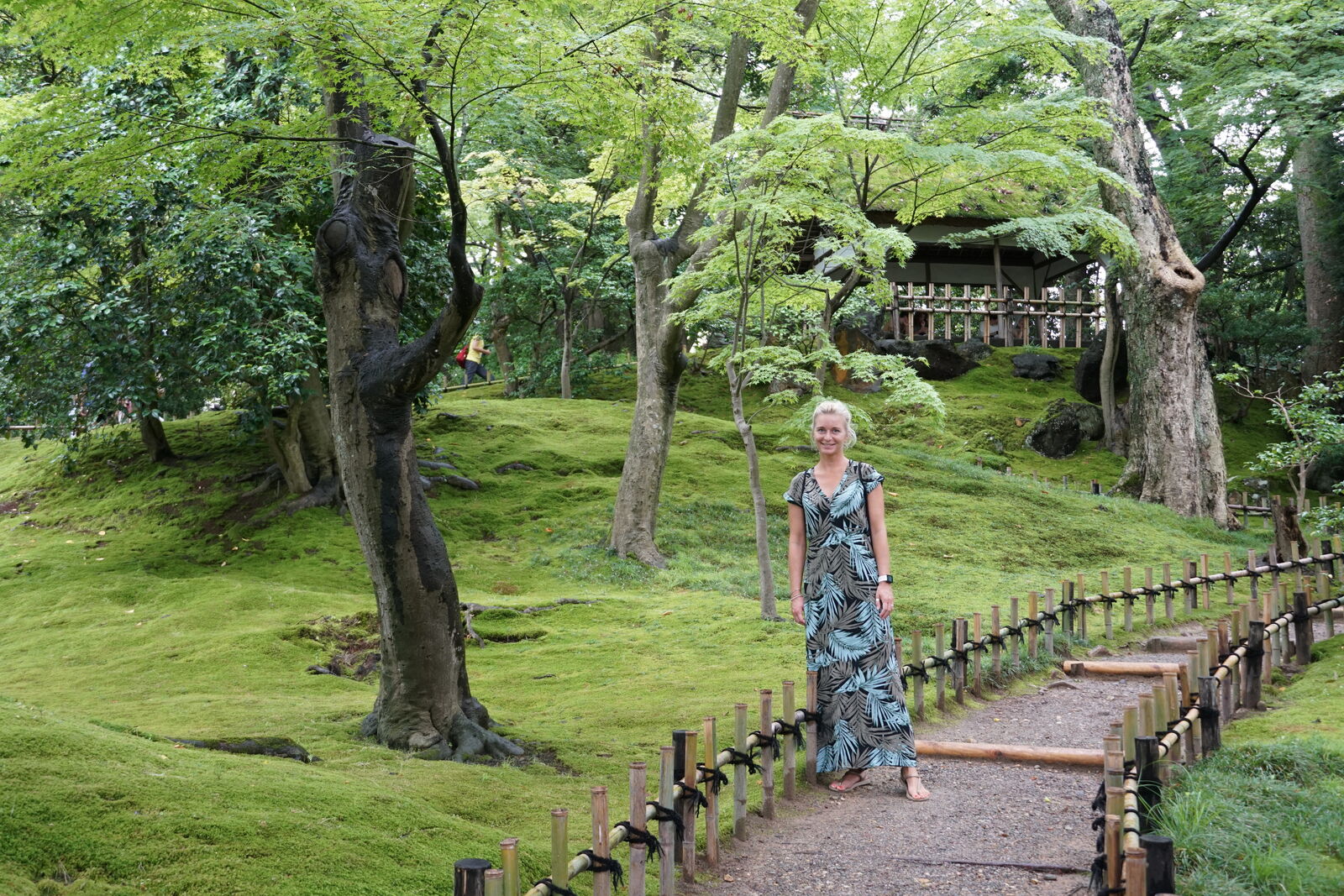 Isi walking along a moss-lined garden path in summer light