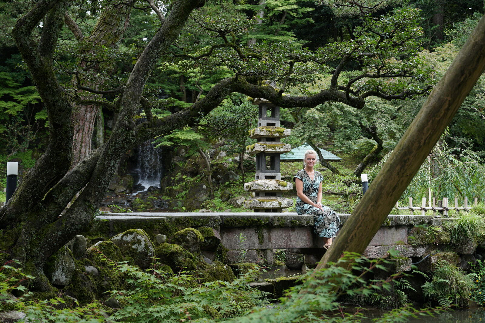 Isi sitting on the ancient stone bridge with stone lantern and waterfall behind her