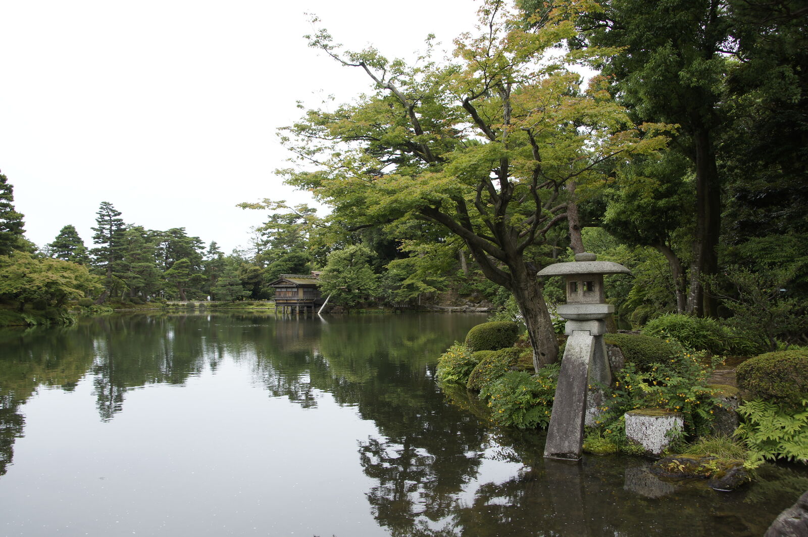 Wide view of Kasumigaike Pond with Kotoji lantern, tea house and tree reflections on overcast day