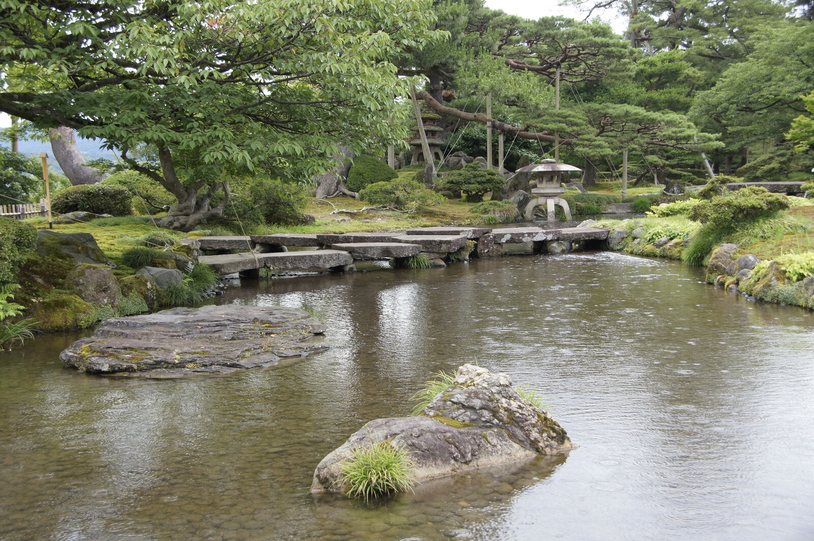 Stone slab bridge crossing the pond with lantern and mossy rock island