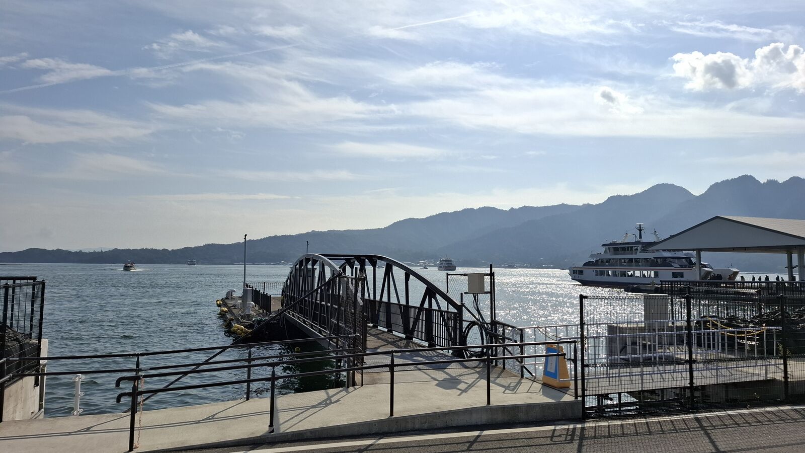 The mainland ferry pier with Miyajima's forested mountains visible across the water, a ferry docked and ready for boarding
