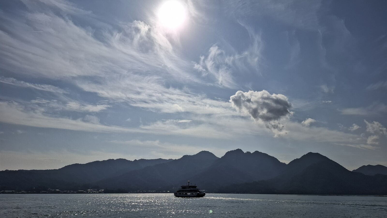 The fast ferry silhouetted against the morning sky with Miyajima's mountain profile rising behind it, backlit clouds creating a dramatic approach