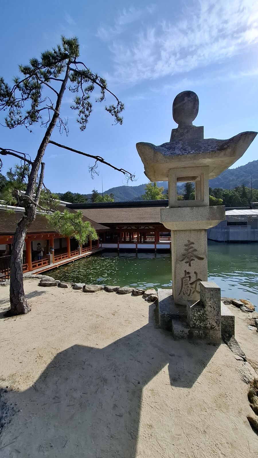 Stone lantern in the foreground with the vermillion shrine buildings visible behind it, water surrounding the structures at high tide