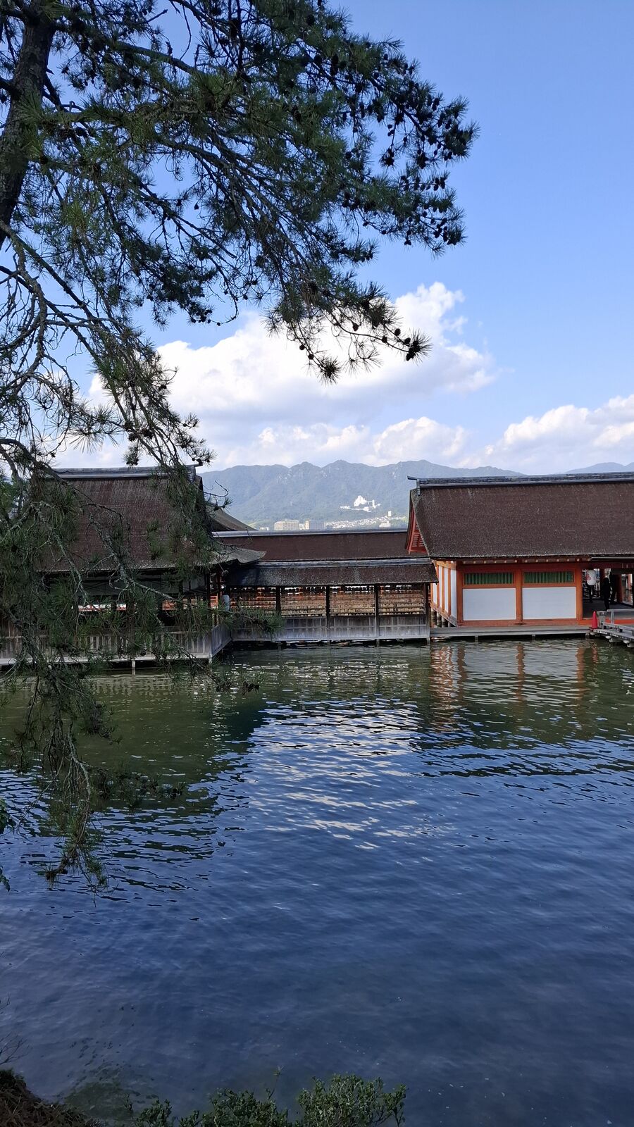 Shrine buildings at high tide, red-trimmed corridors extending over the water, reflections rippling below the wooden walkways