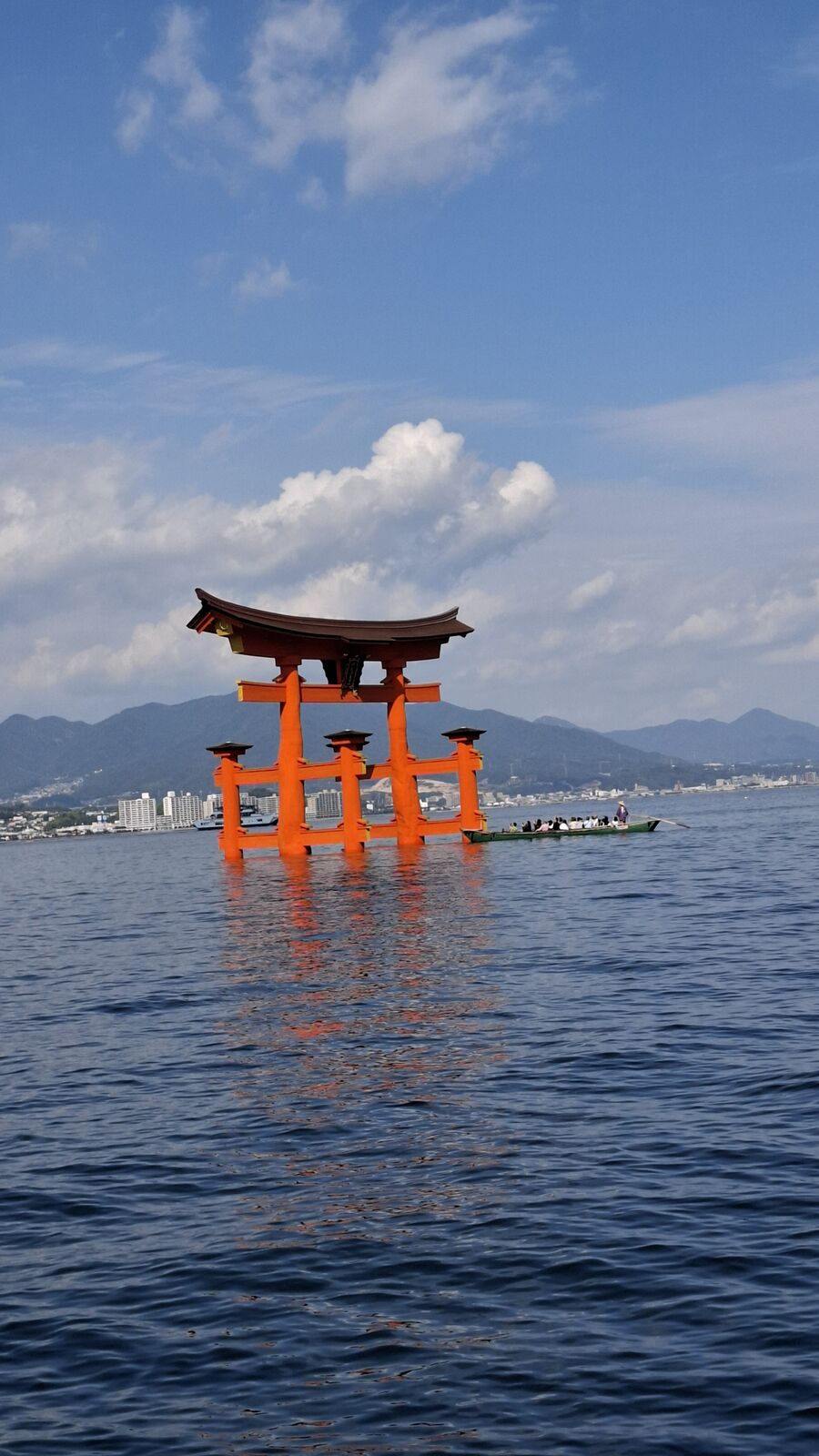 The floating torii of Itsukushima Shrine at high tide, the vermillion gate standing in deep blue water with the forested mountain behind