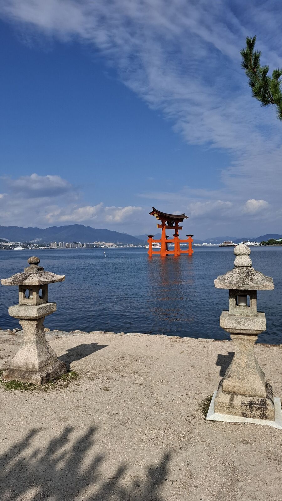 View from the shore toward the torii with stone lanterns in the foreground, the gate standing in receding water as the tide changes