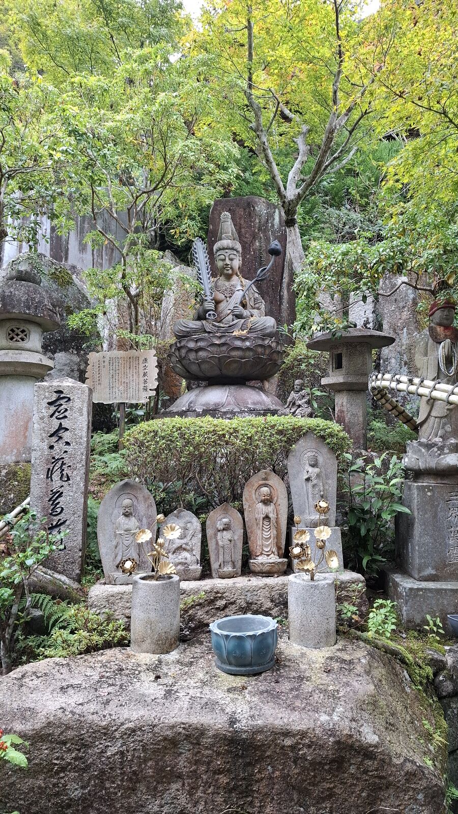 Stone jizo statues with knitted caps along a temple path, the colorful handmade accessories a warm contrast to the grey weathered stone