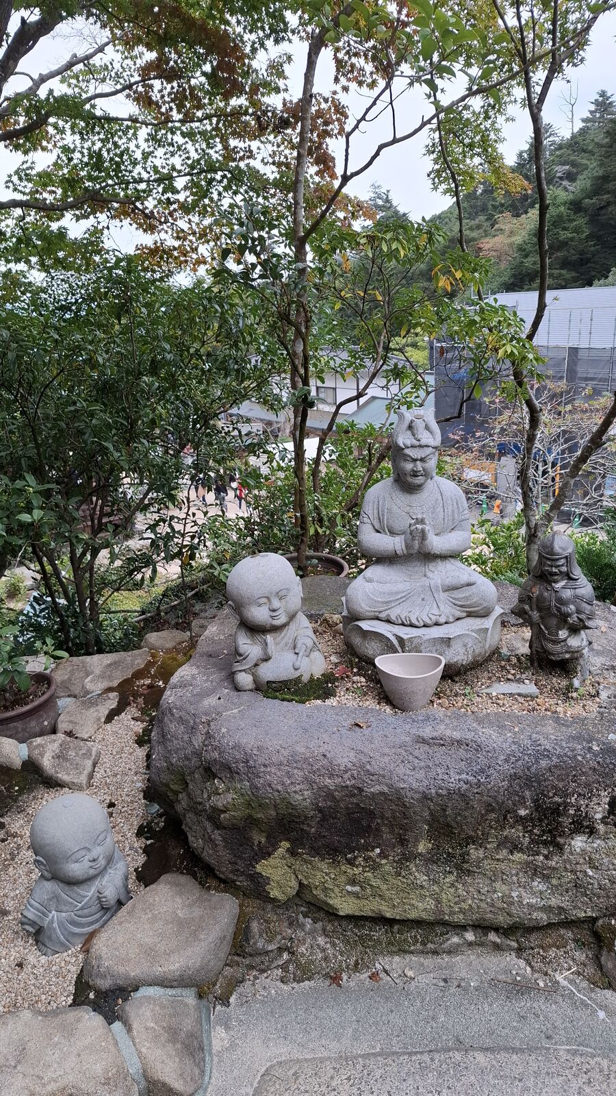 Stone Buddhist statues at Daisho-in, multiple figures arranged among mossy rocks and tree roots on the mountainside, each with a distinct expression