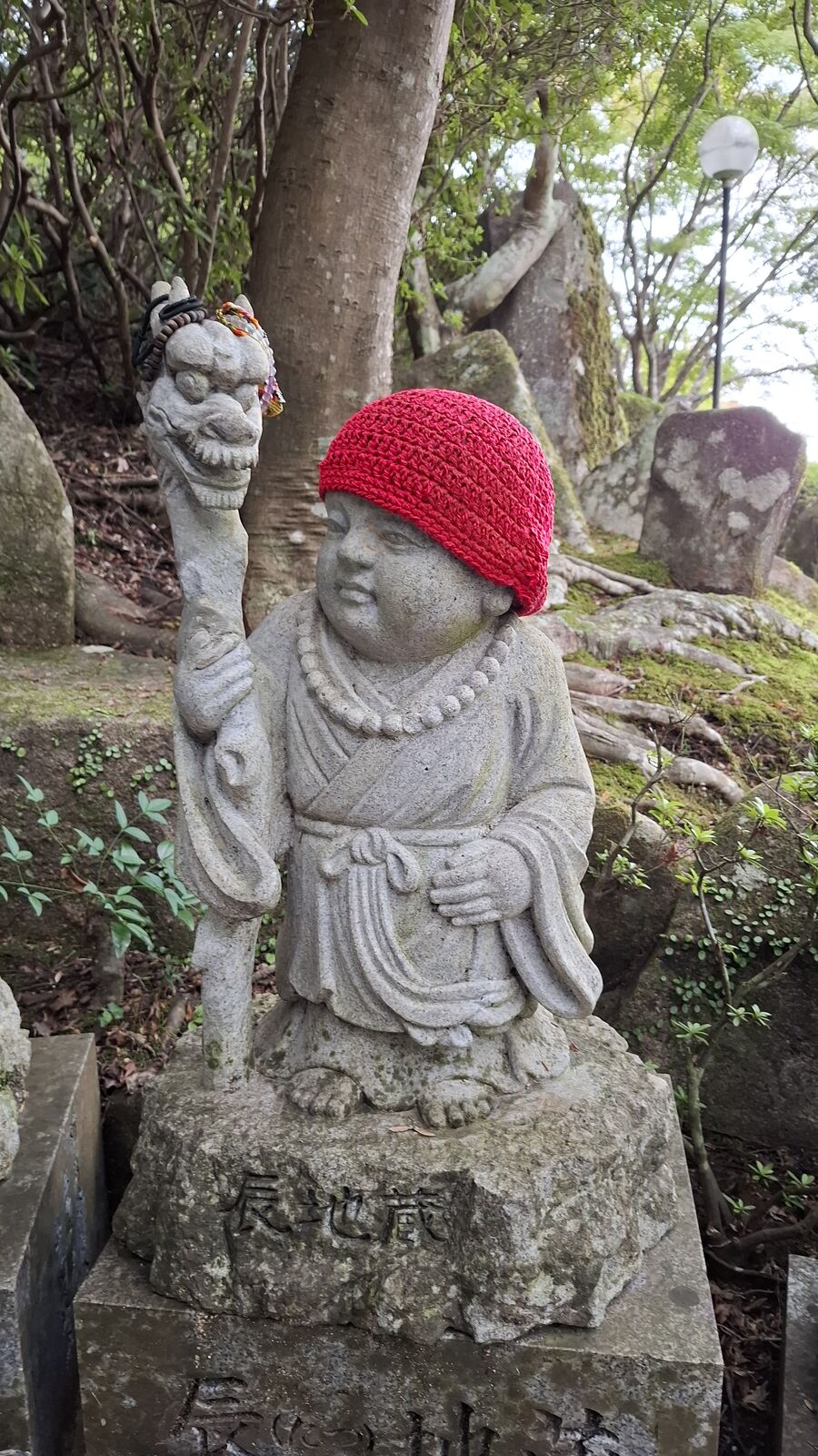Jizo statue wearing a bright red knitted cap, holding a smaller figure, the intimate detail of someone's handwork keeping the stone warm
