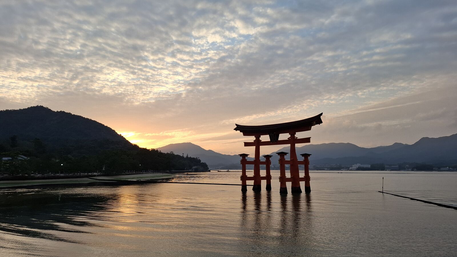 Sunset torii from a slightly different angle, the gate's silhouette reflected perfectly in the calm water, wispy clouds catching the last light