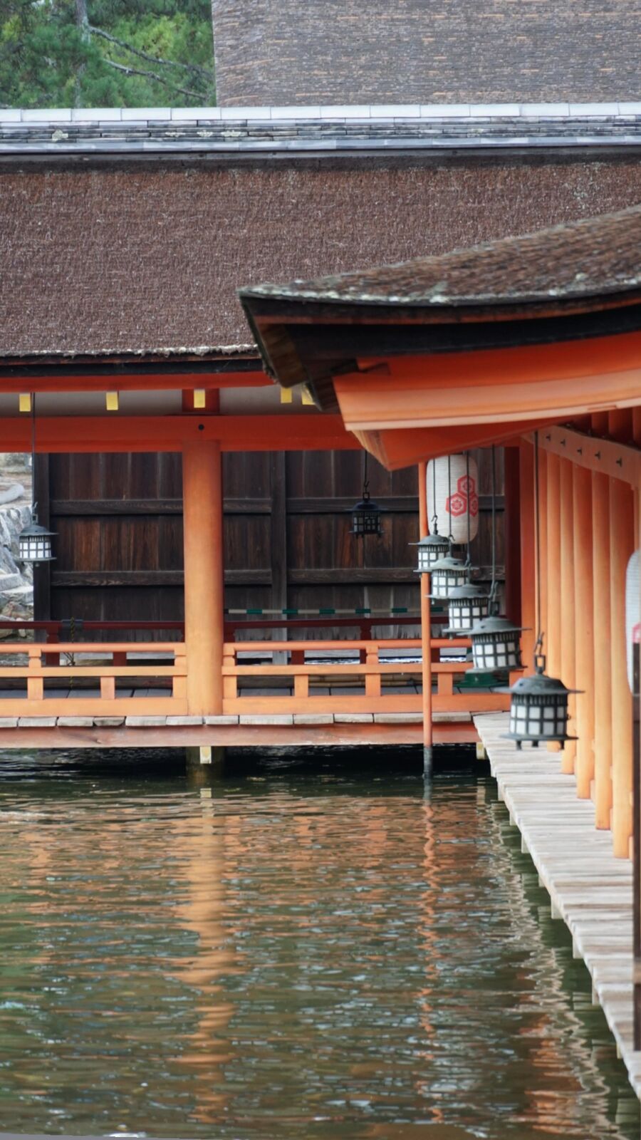 Detail of the shrine corridor: orange pillars and hanging bronze lanterns reflected in the water below, the warm colors doubled by the tide