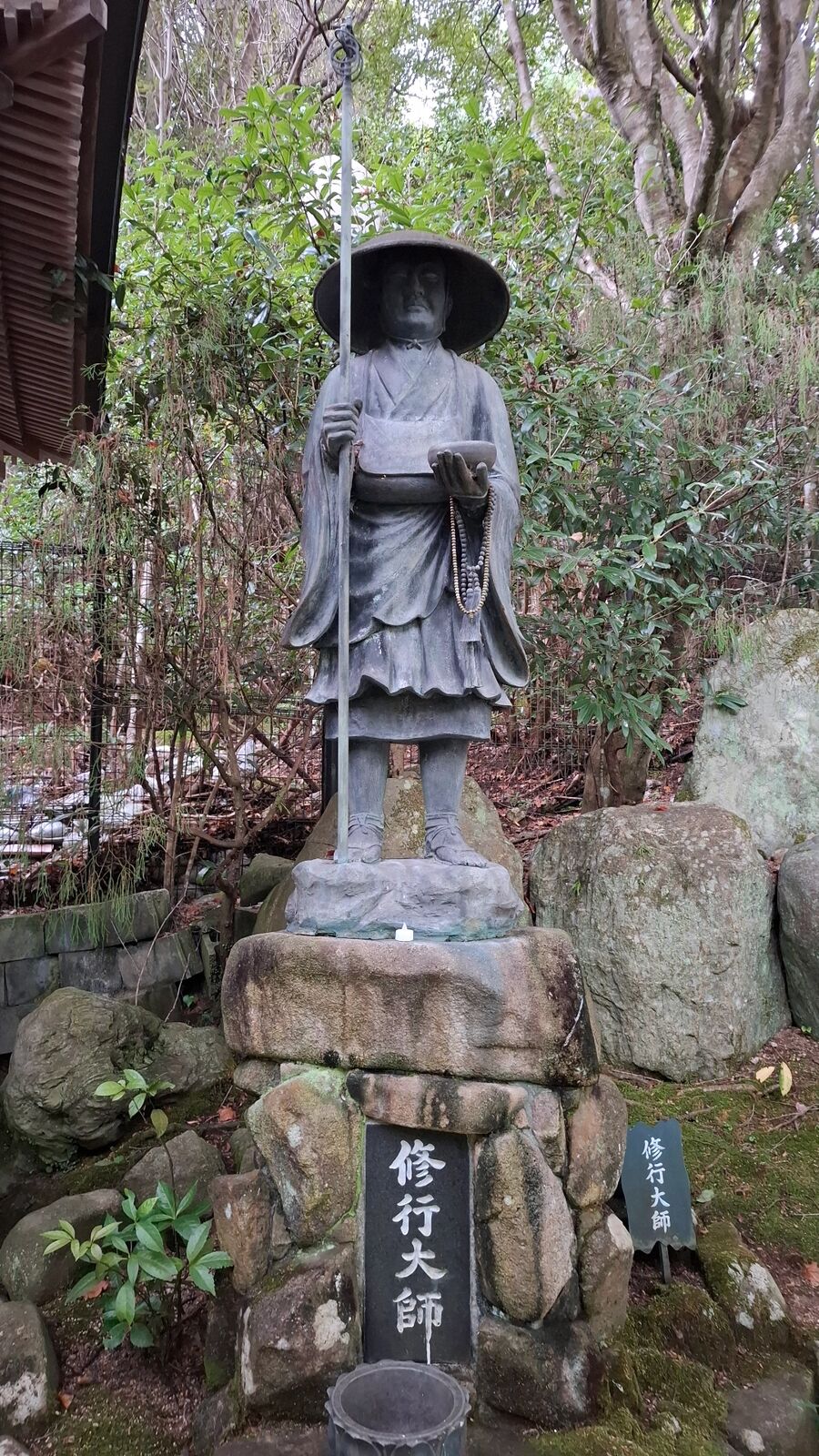Bronze statue of Kobo Daishi in traveling robes with a walking staff, the founder of Shingon Buddhism, standing on the path toward Mount Misen