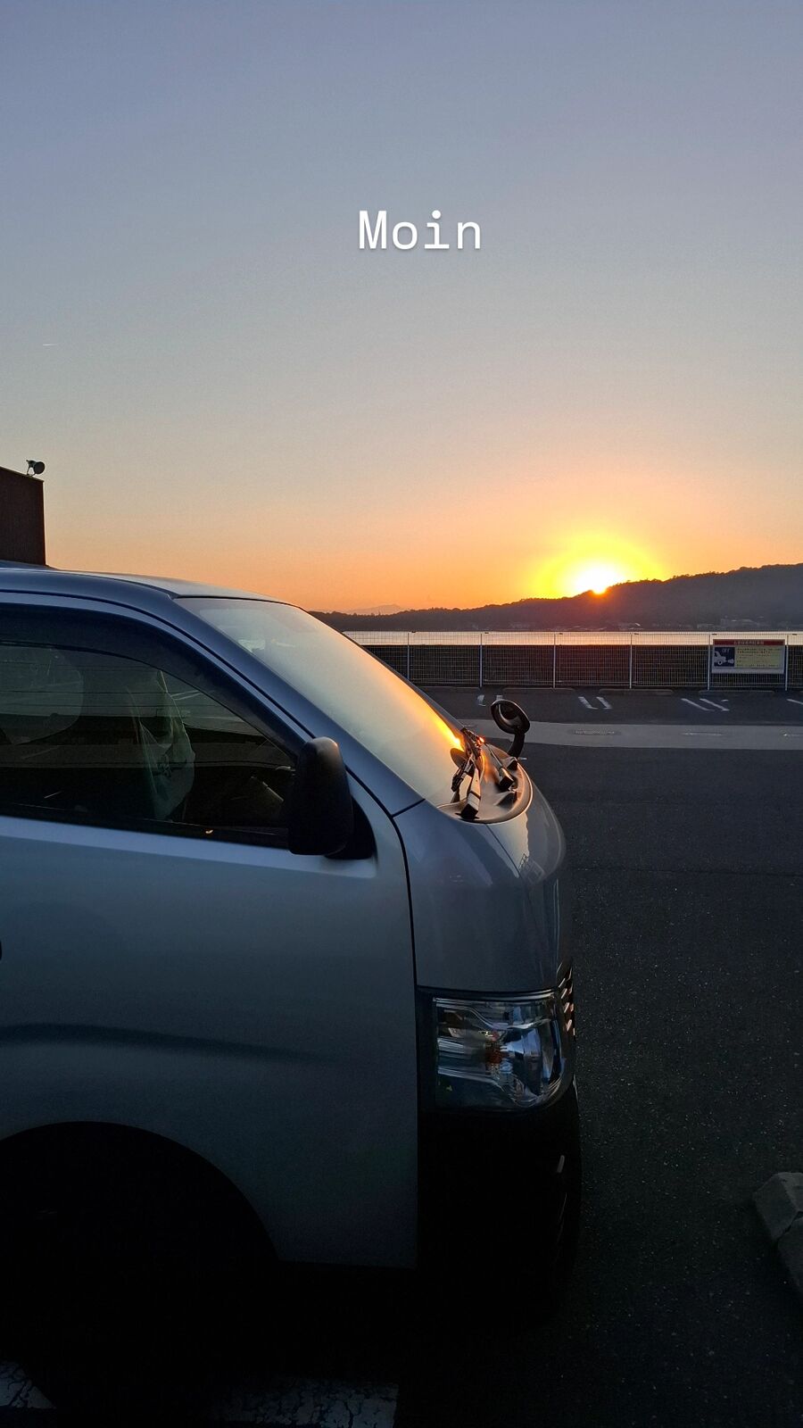 Next morning: the van parked at the mainland lot near the ferry terminal, sunrise over the Inland Sea visible behind it, a new day beginning