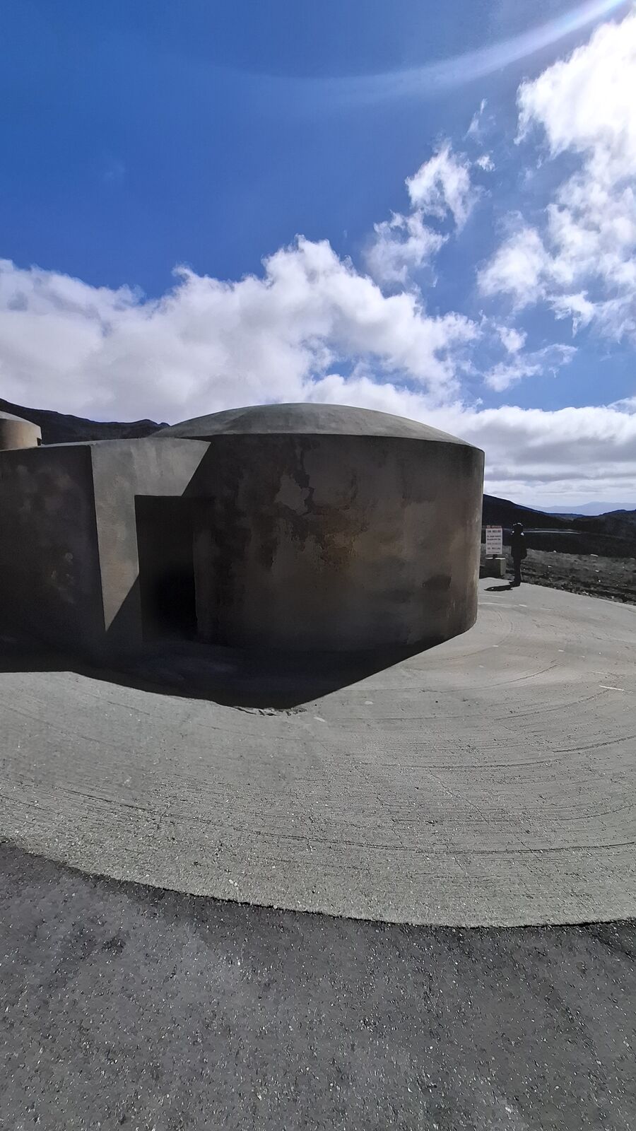 Concrete evacuation bunker on the volcanic plain, a half-dome shelter built to protect visitors from sudden eruptions, grey ash covering the ground around it