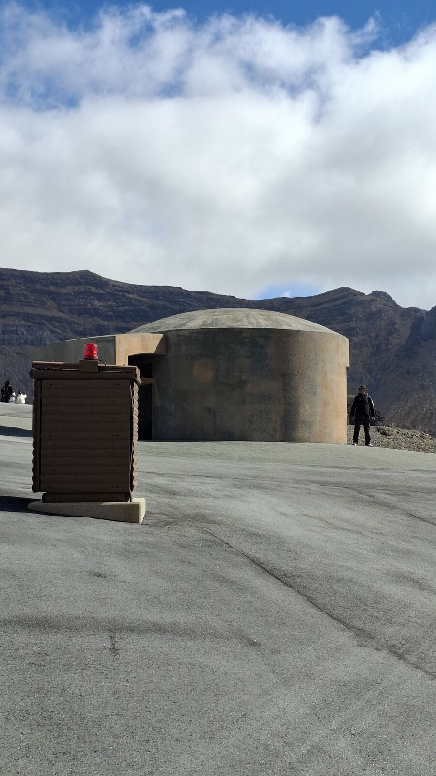 Close-up of an evacuation bunker entrance with emergency equipment box, the barren volcanic landscape stretching behind it