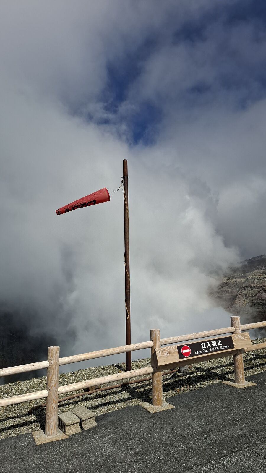 Red windsock streaming in the volcanic wind, gas drifting past the Keep Out barrier, the crater wall looming behind in layers of grey rock