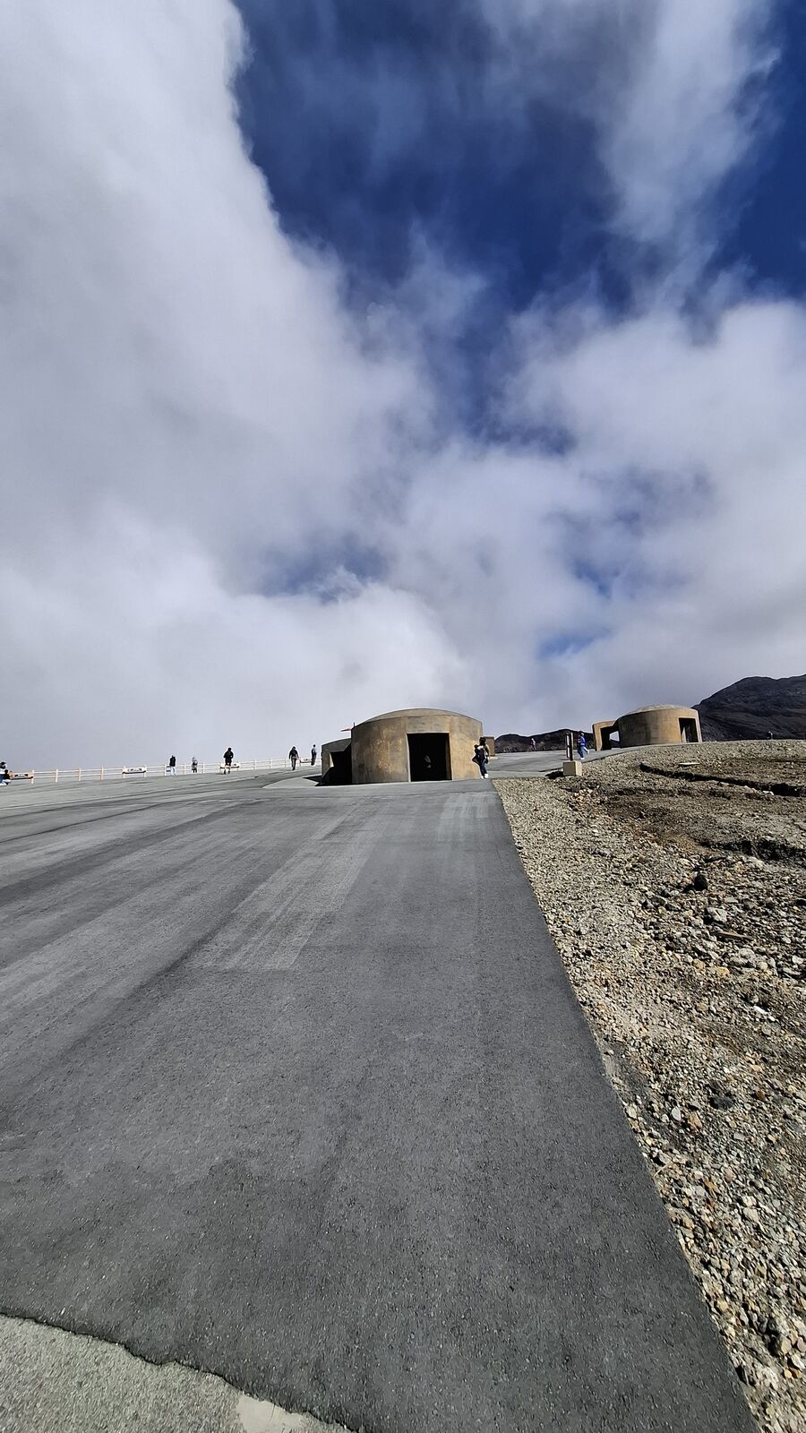 The volcanic walkway stretching across the moonscape, concrete bunkers visible in the distance, the barren terrain emphasizing the scale of the caldera