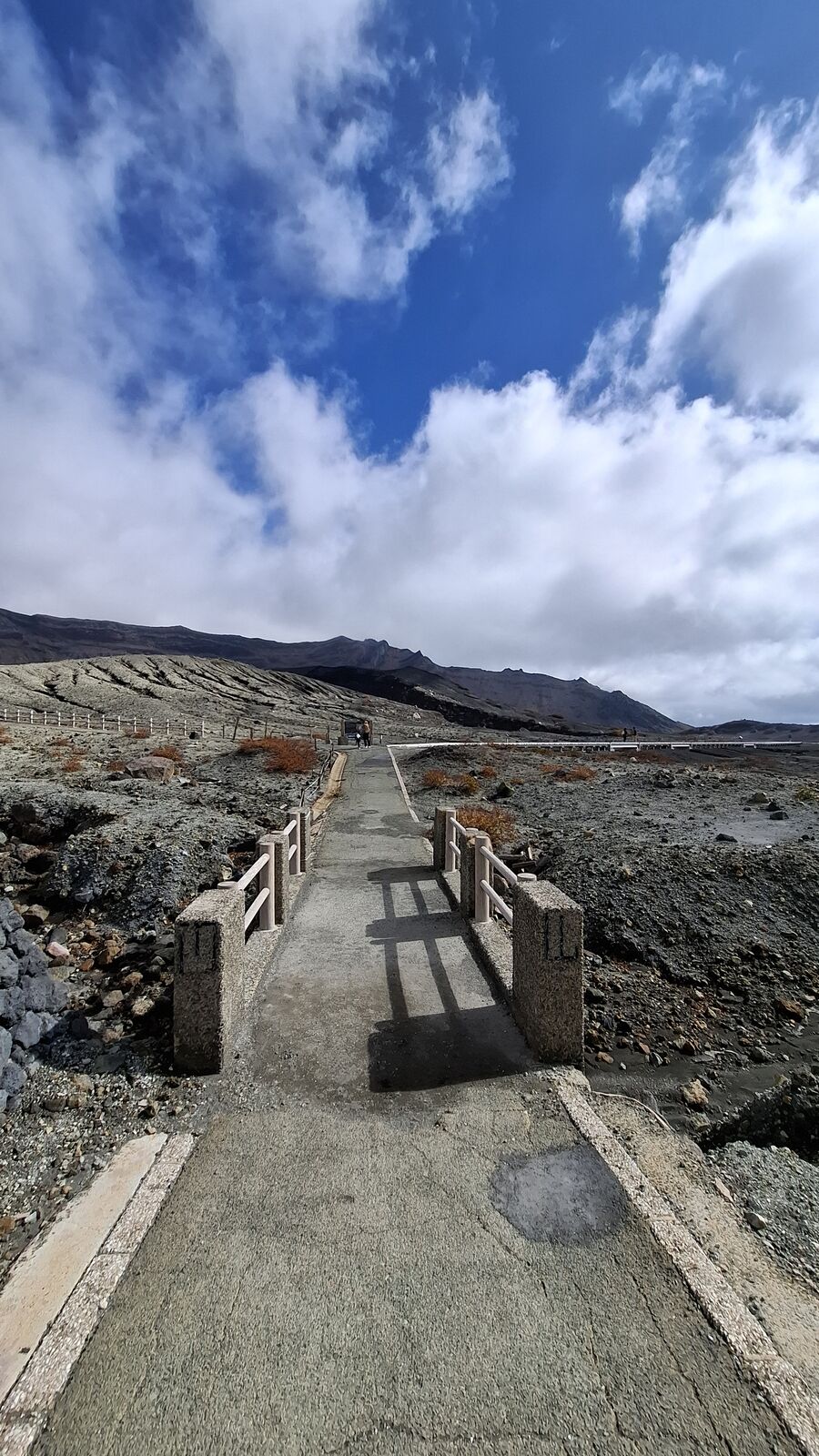 Boardwalk with metal railings crossing the volcanic desert, crater rim in the background, the careful infrastructure built to let visitors walk safely through an active volcanic zone