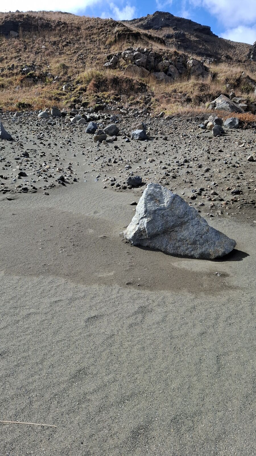 Close-up of a volcanic rock emerging from fine grey ash, the texture of cooled lava sharp against the smooth surface of the volcanic sand
