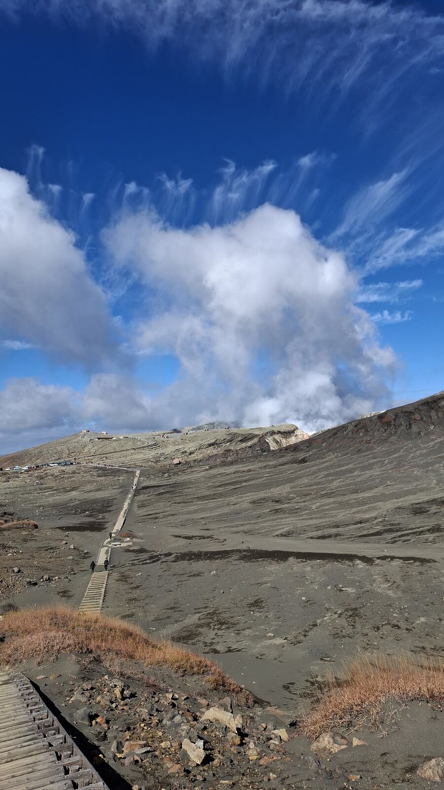 Paved path cutting through the volcanic ash desert toward the steaming crater, boardwalk railings leading the eye into the distance