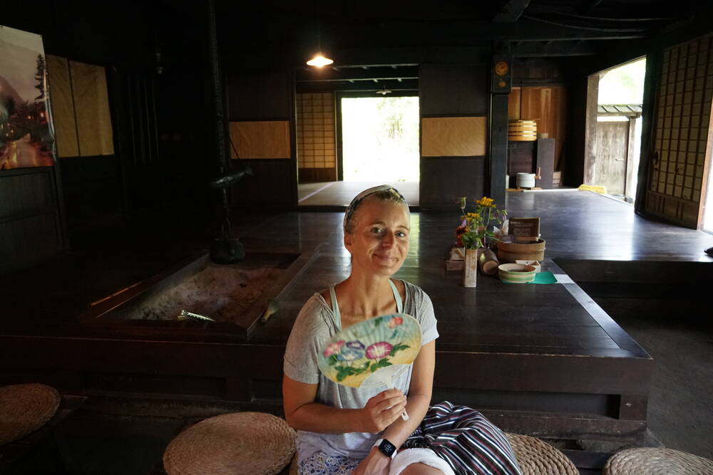 Inside the tea station: dark wooden beams, an irori hearth in the floor, shoji screens, and warm light from the open windows